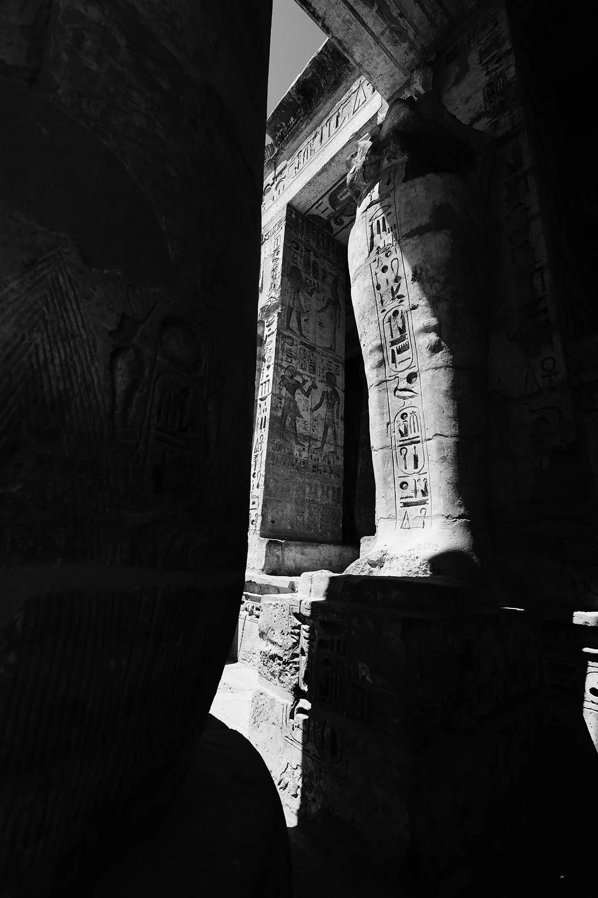 Colonnes et murs d'un temple antique égyptien avec des hiéroglyphes gravés, en partie dans l'ombre, avec la lumière naturelle qui éclaire certains détails.