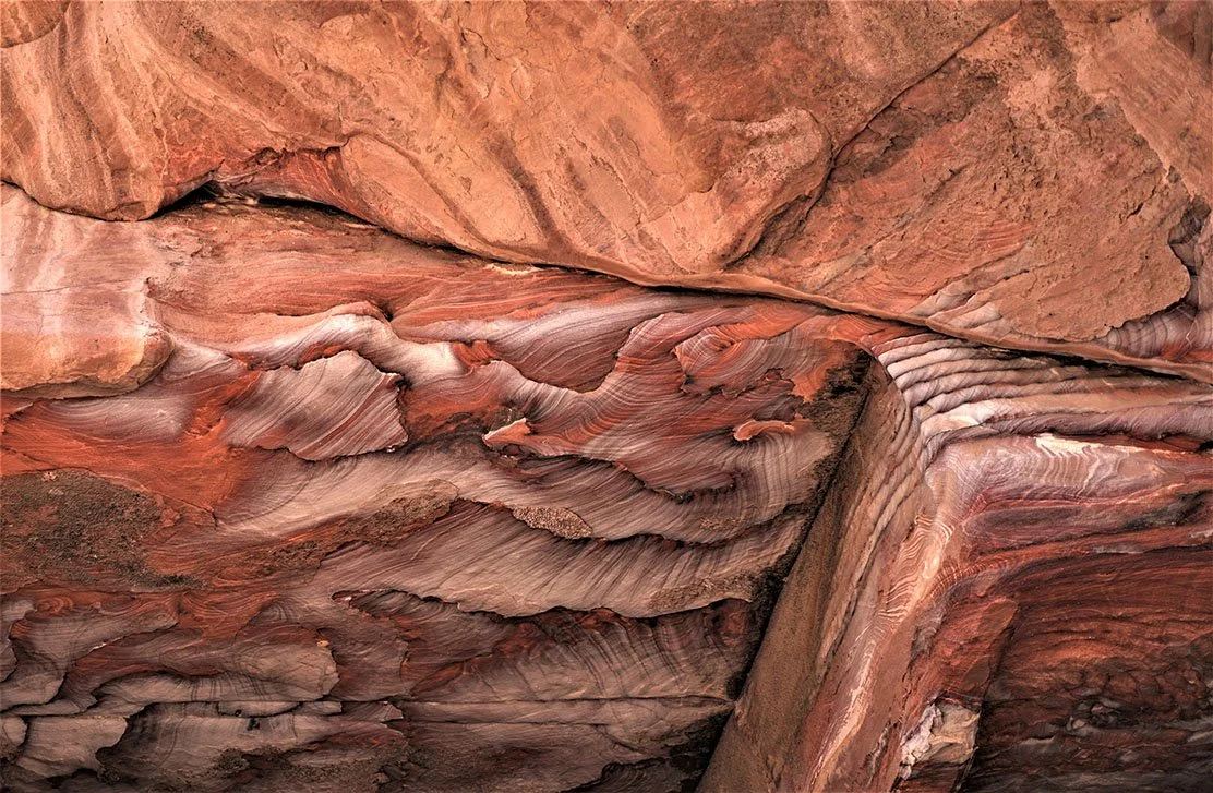 Roches aux couleurs rouges, roses et blanches avec des formes caillouteuses et laminées.