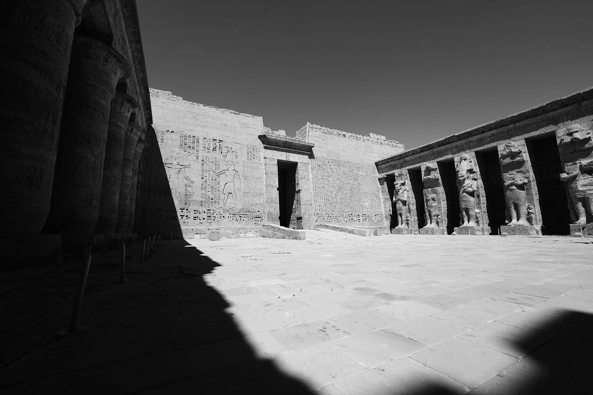 Vue d'une ancienne site archéologique égyptien avec colonnes ornées de hiéroglyphes et statues de figures égyptiennes en pierre.