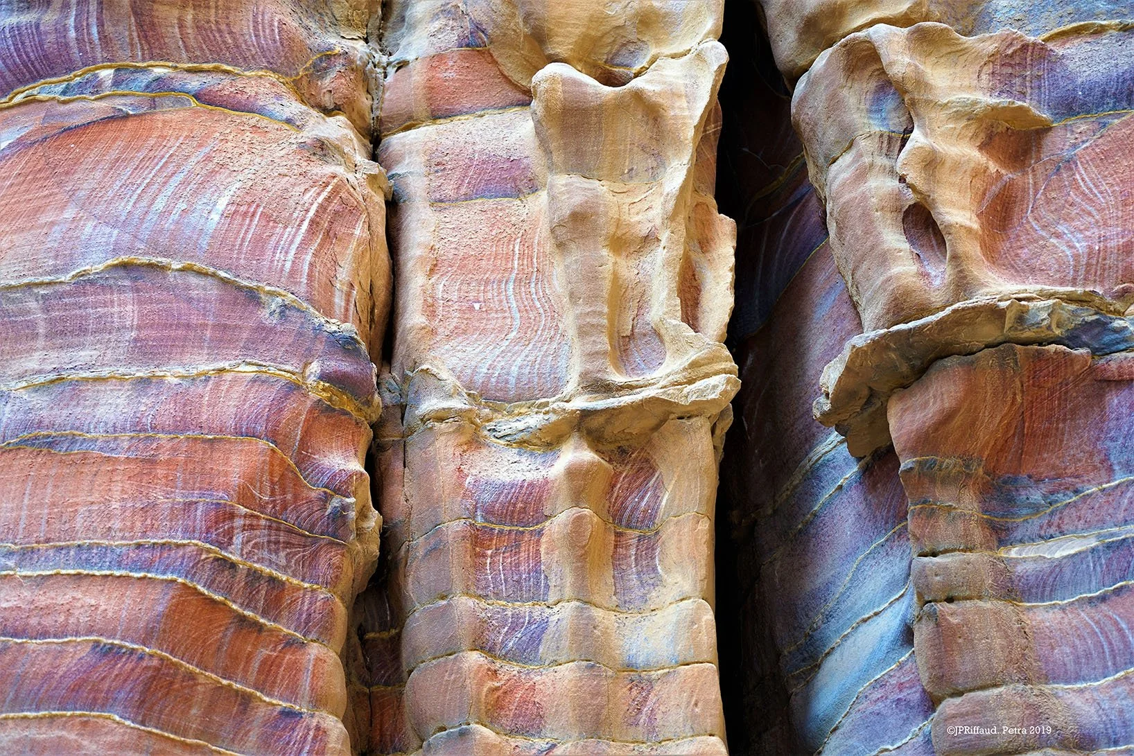 Surface de roches colorées avec des couches stratifiées en teintes rose, orange, violet et beige.