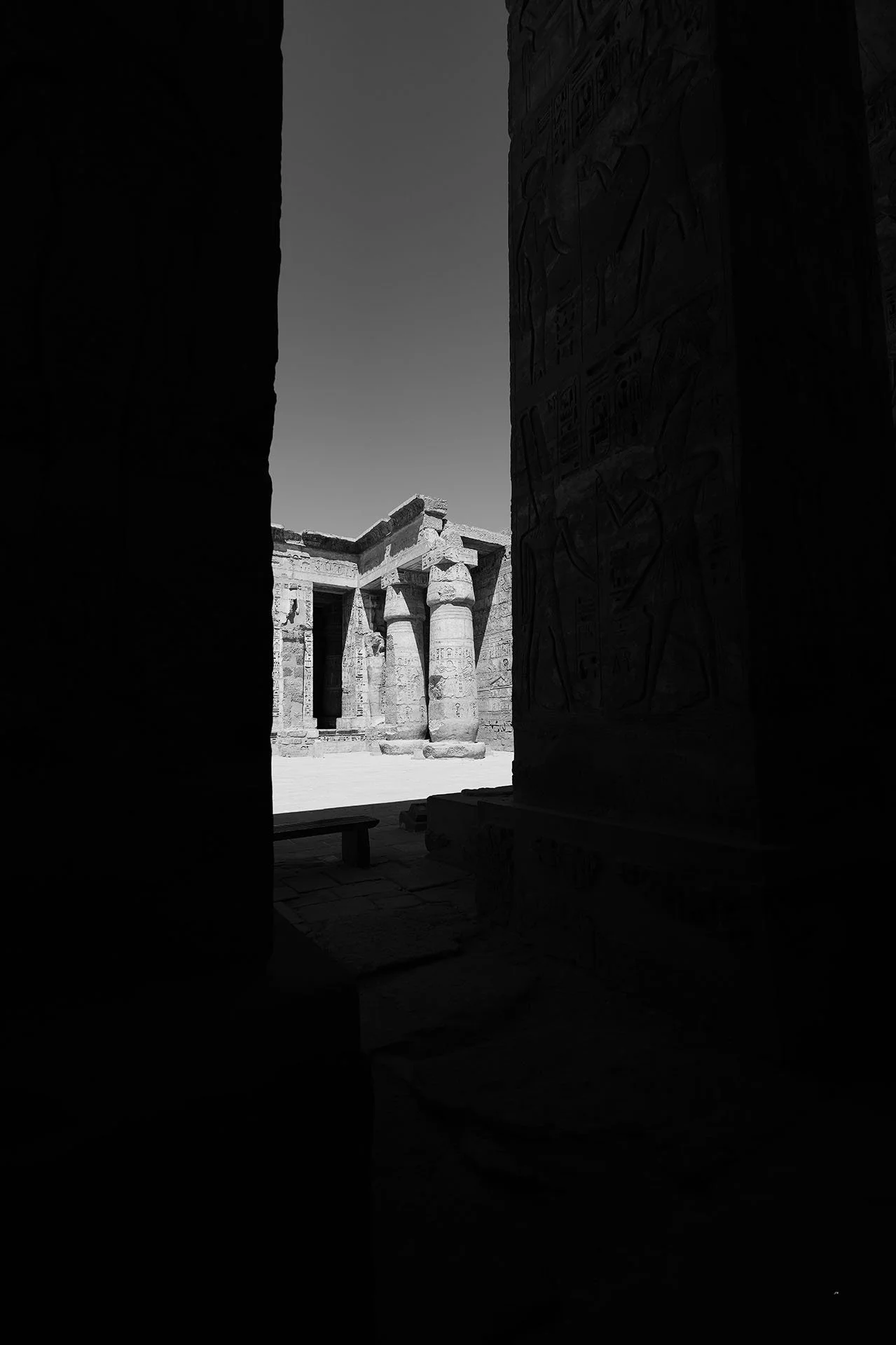 Vue d'un temple égyptien ancien avec des colonnes massives et des hiéroglyphes, vue depuis un passage sombre vers une zone éclairée.