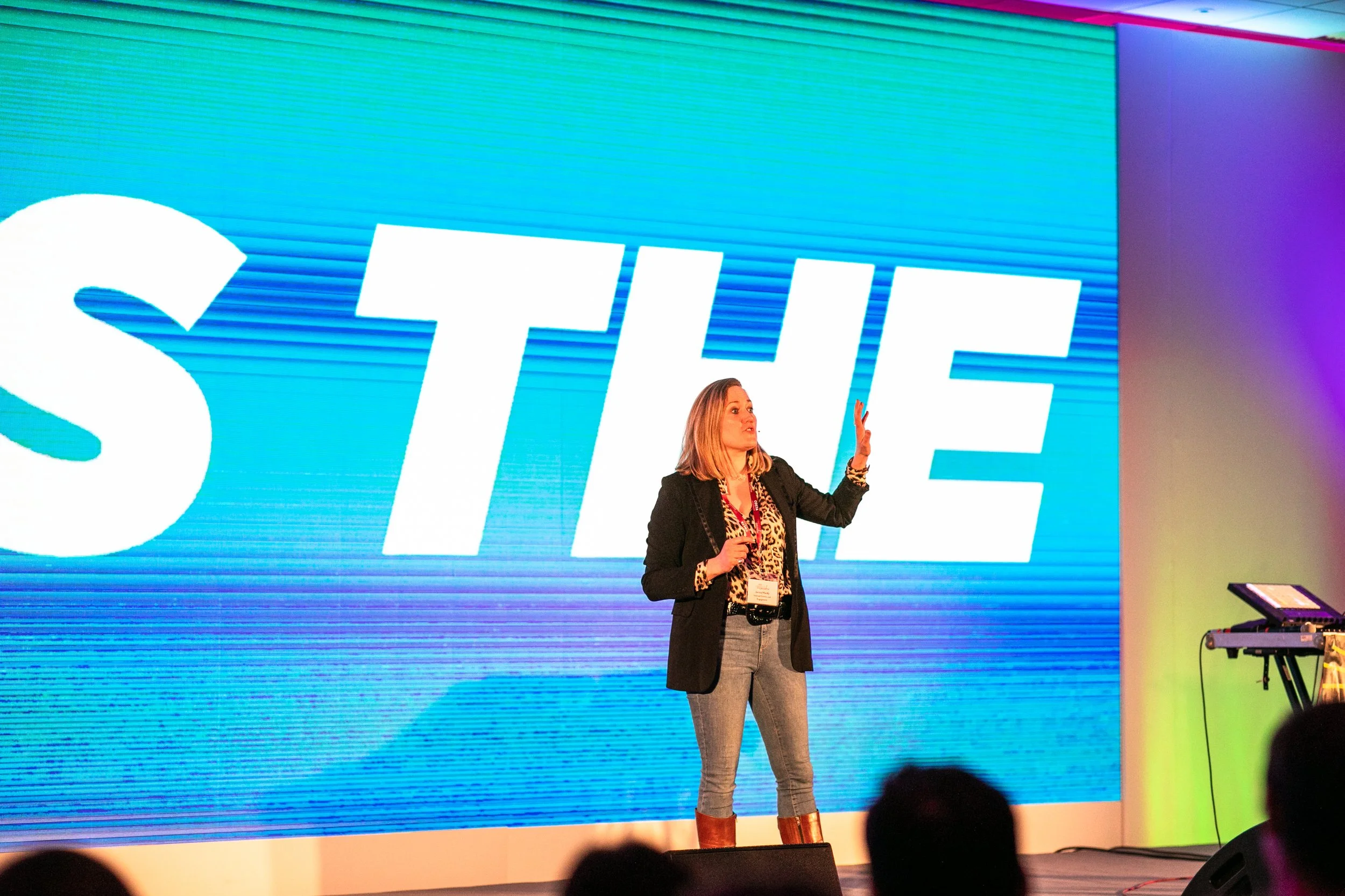 A woman on stage giving a presentation in front of a large screen that says 'STYLE' in big white letters, with colorful lighting.