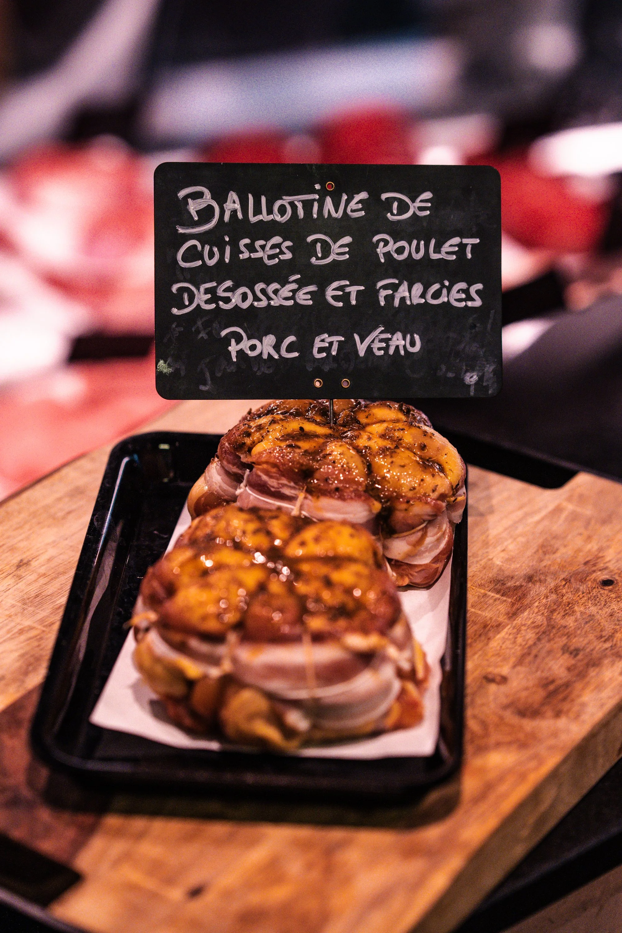 Gros plan d'une assiette avec des morceaux de poulet désossé, farcis, recouverts de sauce et garnis de noix de pécan, avec un tableau noir portant une inscription en français sur la nourriture.
