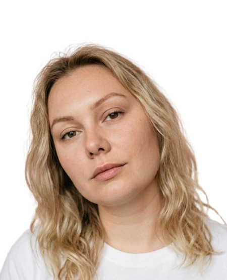 Close-up of a young woman with blonde hair and fair skin, looking directly at the camera with a neutral expression.