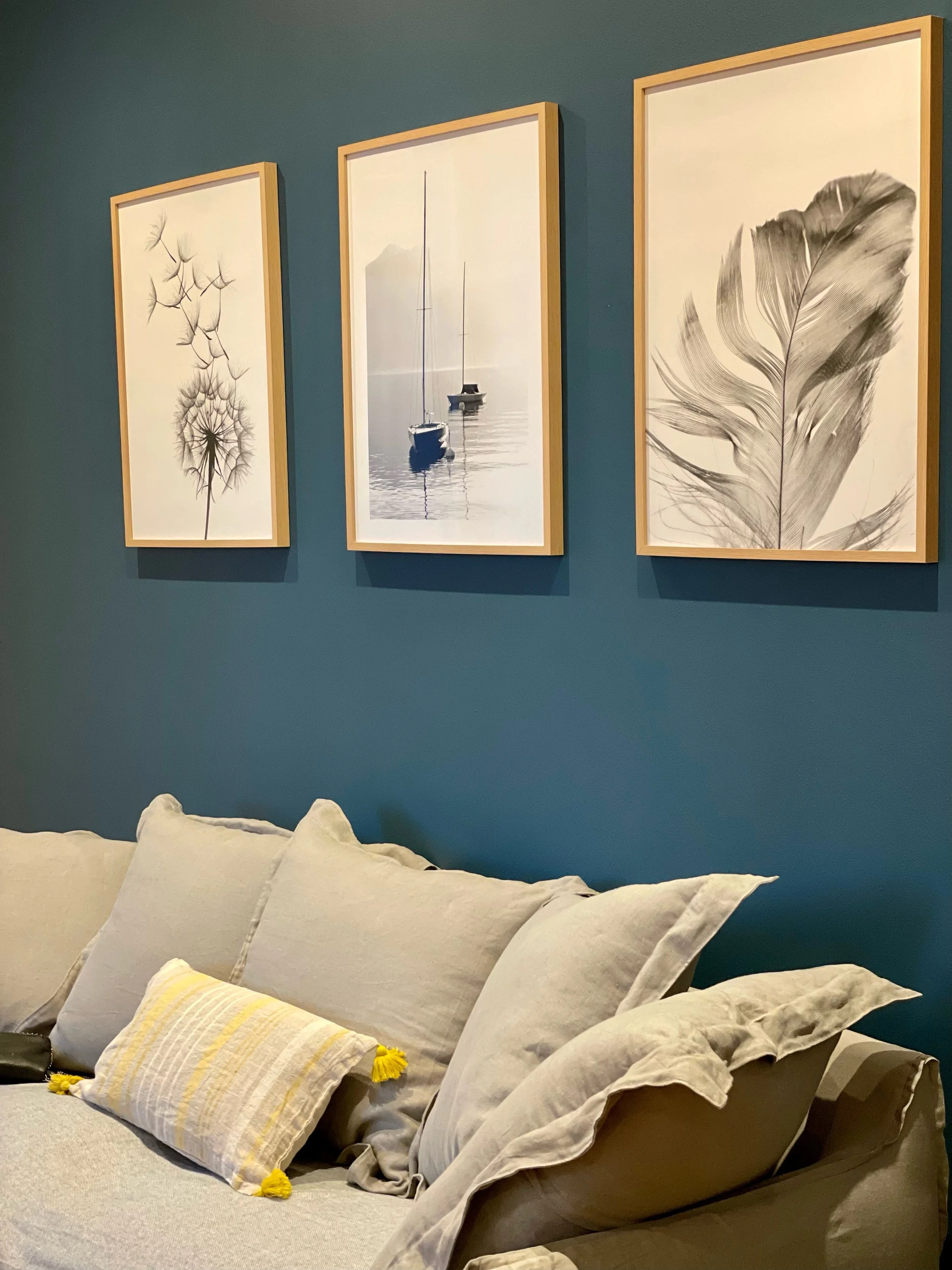 Un mur bleu avec trois cadres de photos en noir et blanc représentant des éléments naturels, au-dessus d'un canapé beige avec plusieurs coussins