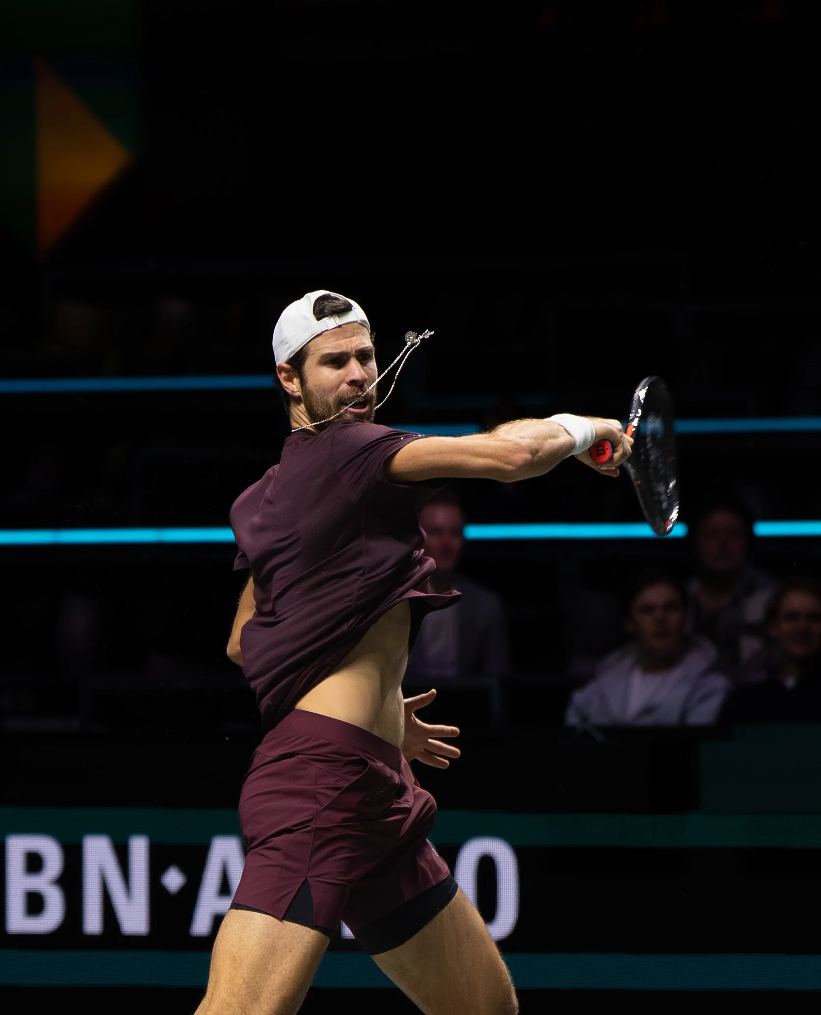 Karen Khachanov hitting a tennis ball during a match, with spectators watching in the background.