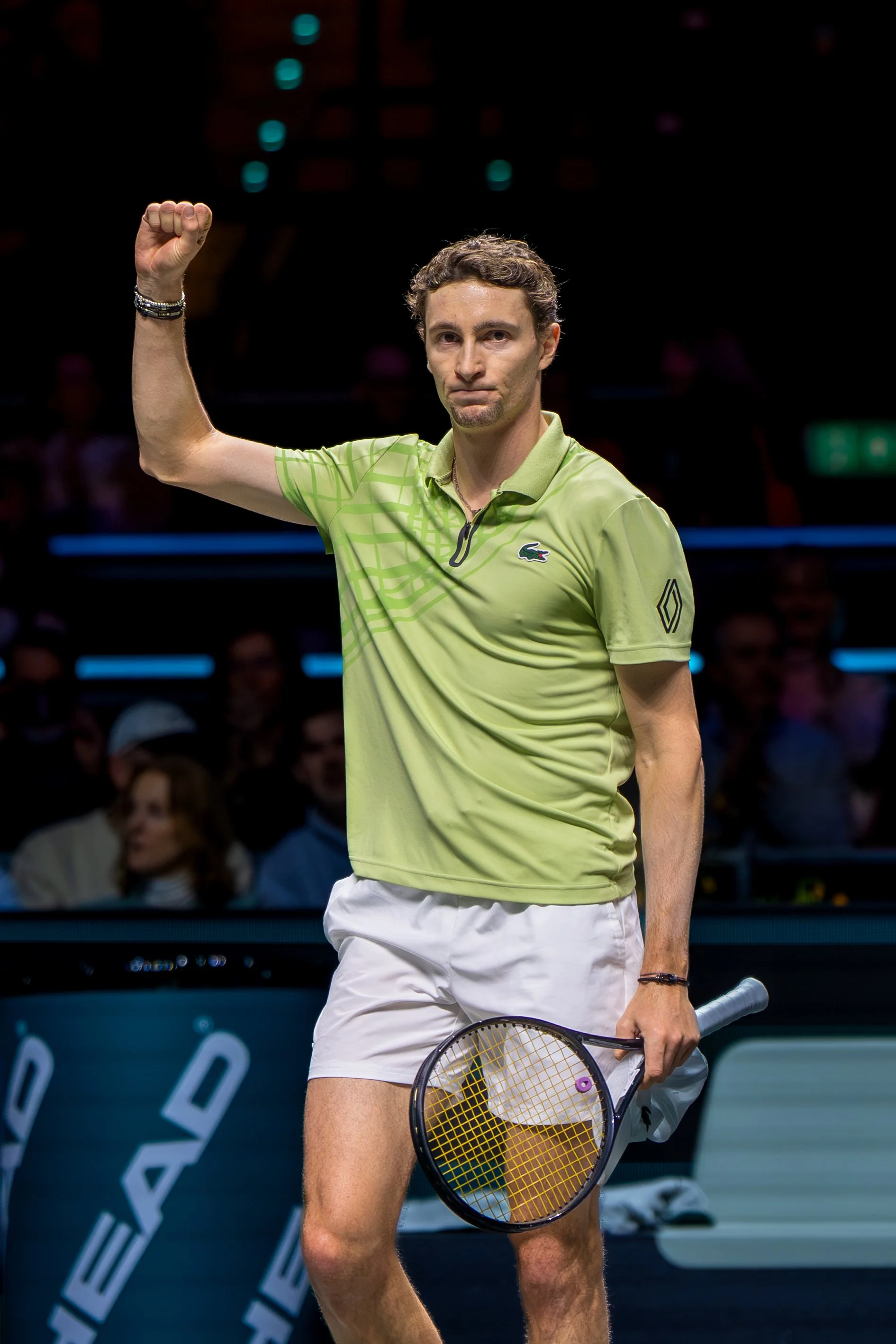 Ugo Humbert holding a tennis racquet in his left hand, raising his right fist in celebration during a match.