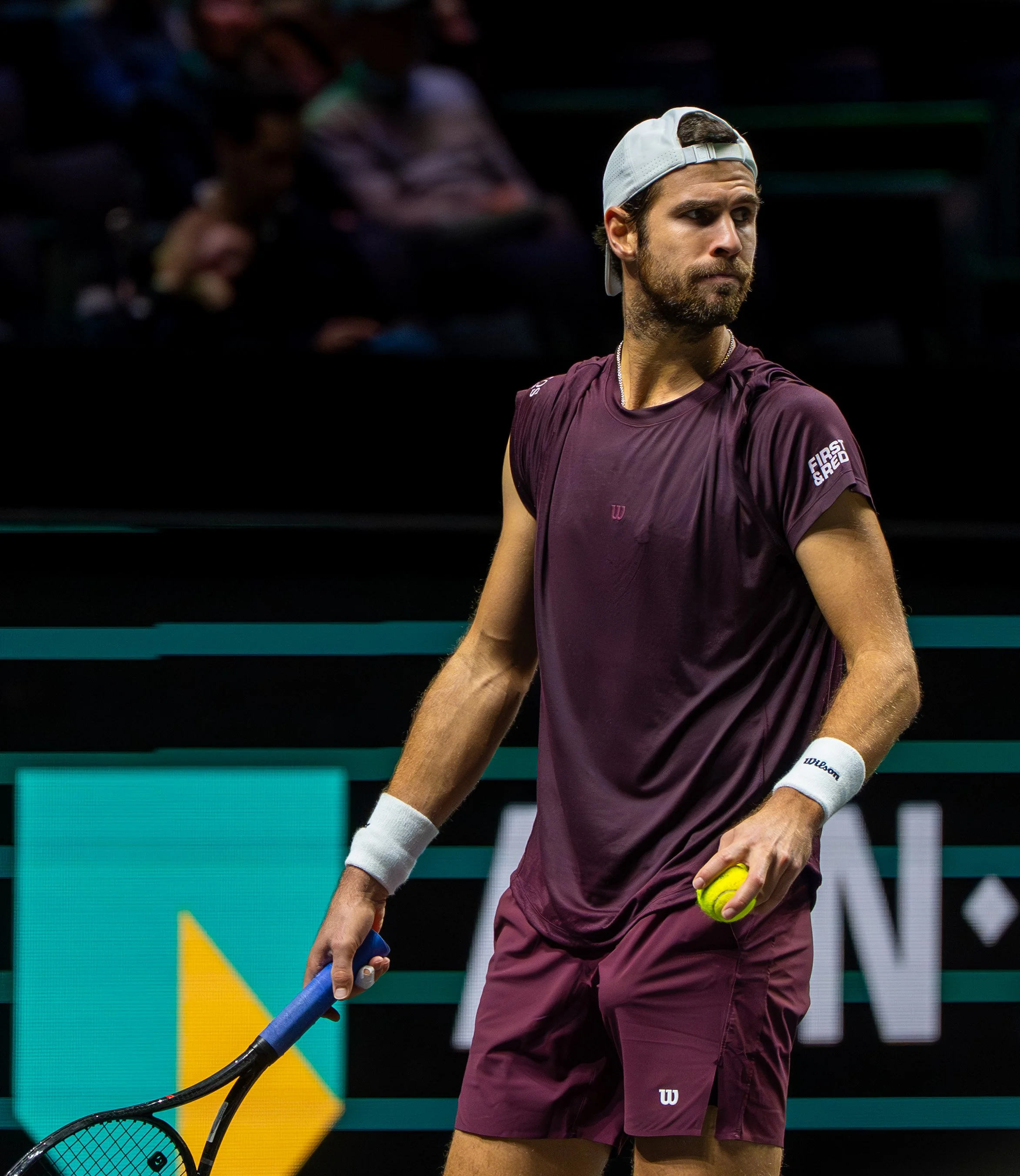 Karen Khachanov holding a tennis ball and a racket on a tennis court.