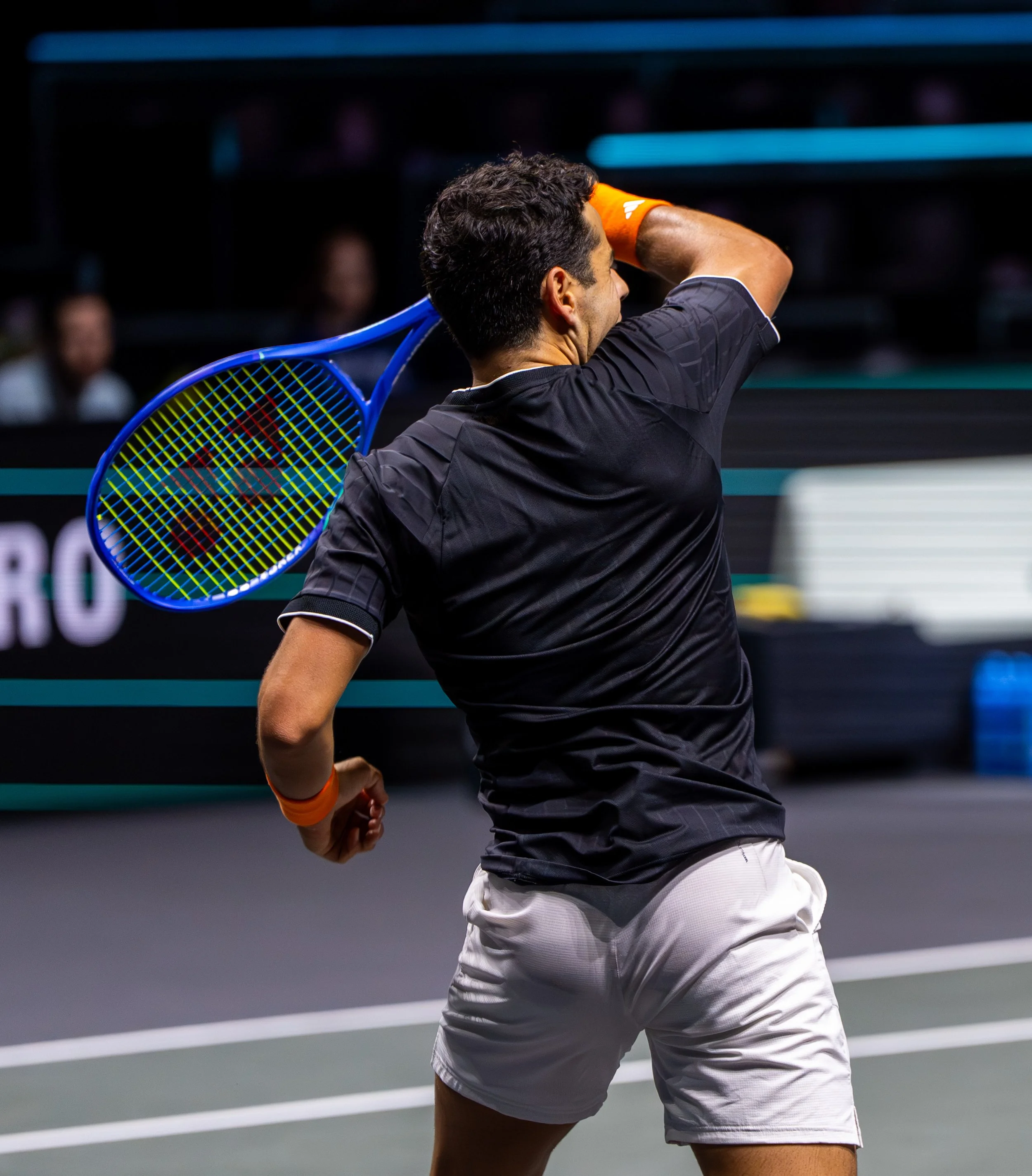 Jaume Munar wearing a black shirt and white shorts hitting a tennis ball during a match, holding his racket over his shoulder.