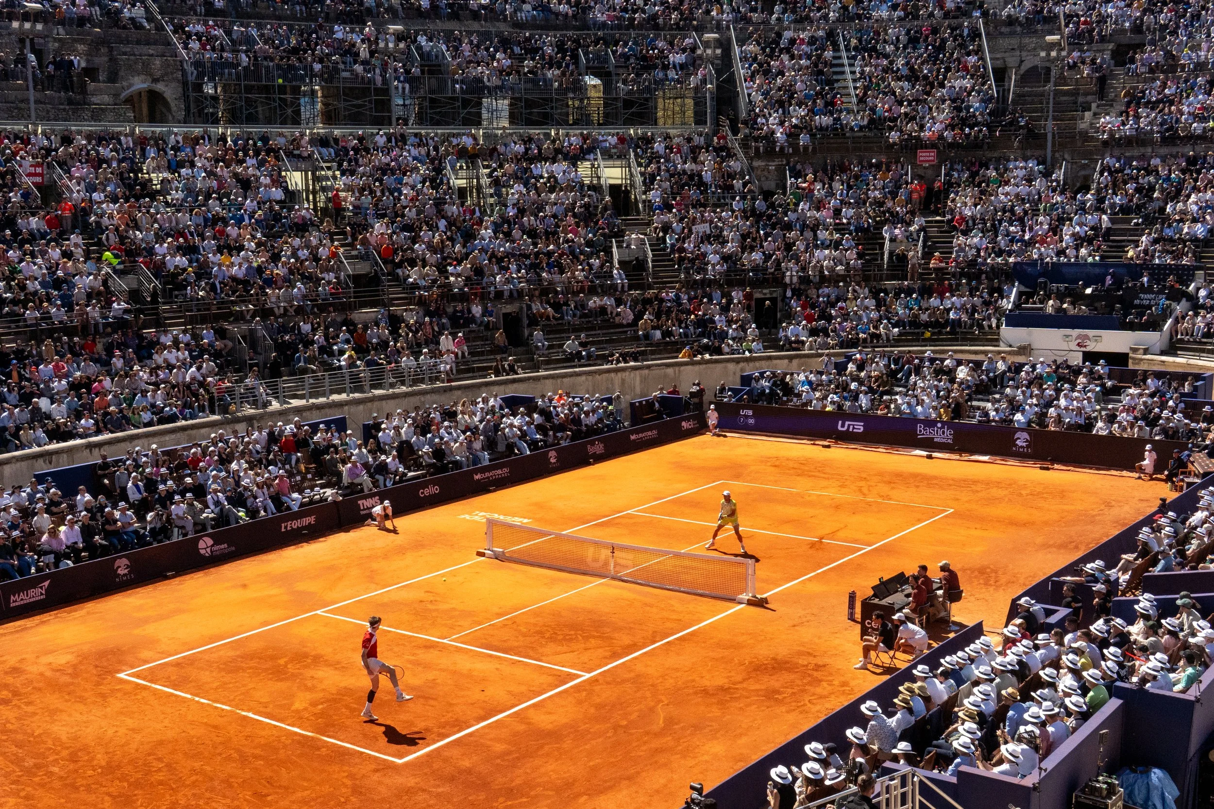 A tennis match on a clay court with two players, surrounded by a large audience in a stadium.