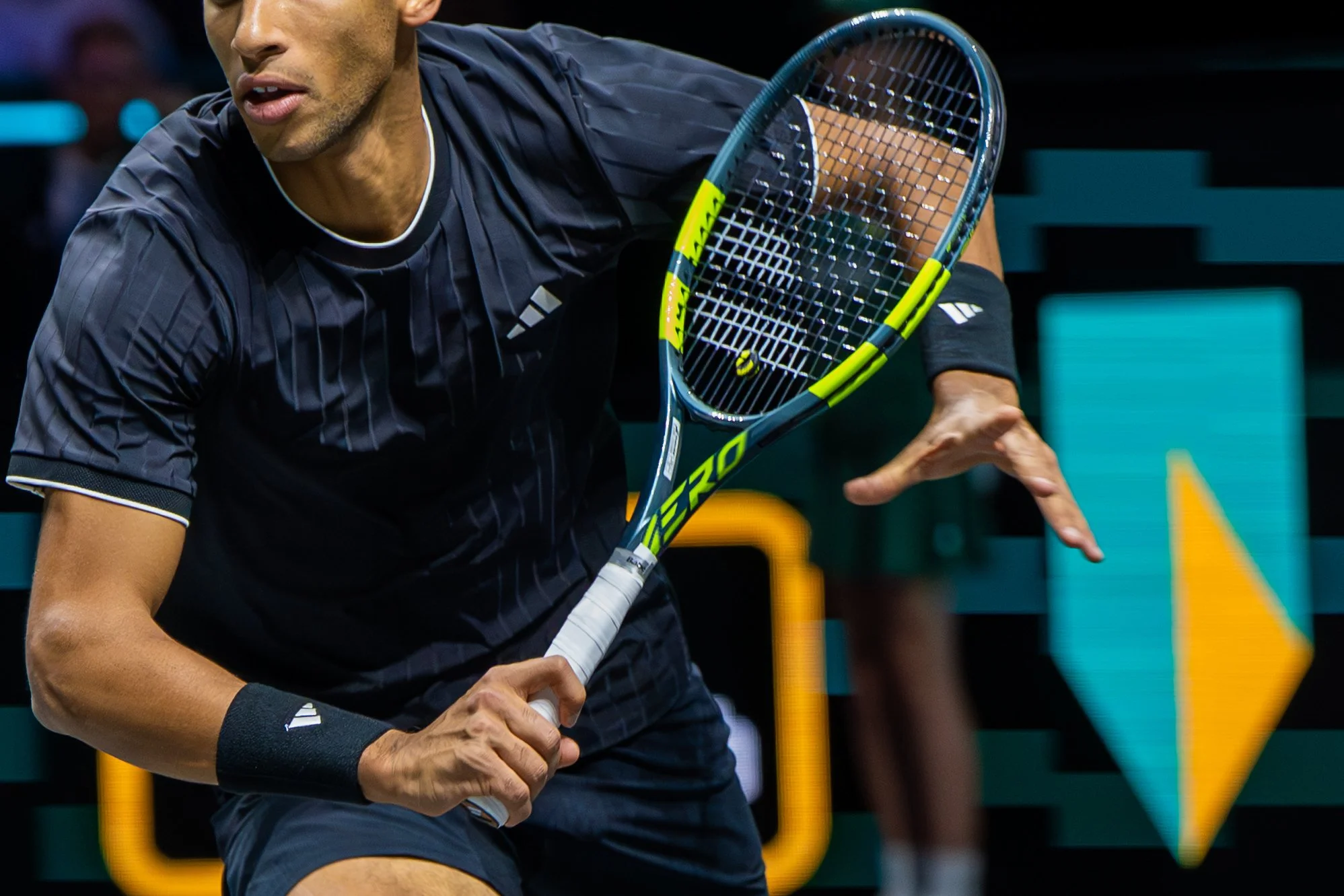 Felix Auger-Aliassime holding a tennis racket, preparing to hit a shot on a tennis court during a match.