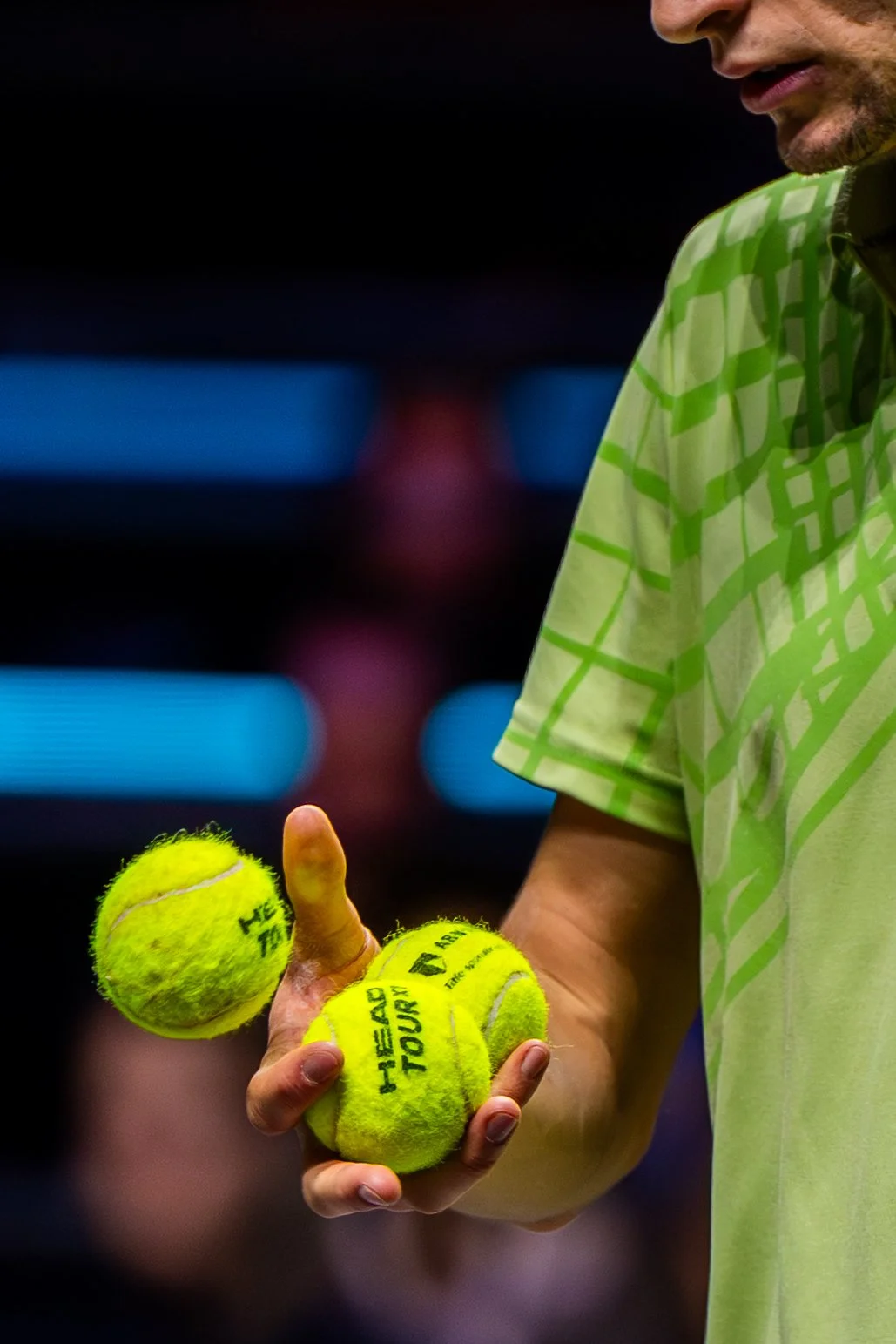 Ugo Humbert holding three yellow tennis balls with the label "HEAD TOUR" and a thumb pointing up in a sports arena.