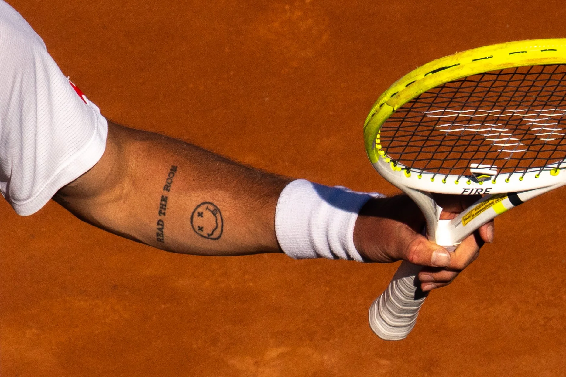Corentin Moutet on a tennis court wearing a white sleeve on their arm, holding a tennis racket with a yellow and white frame and black strings.
