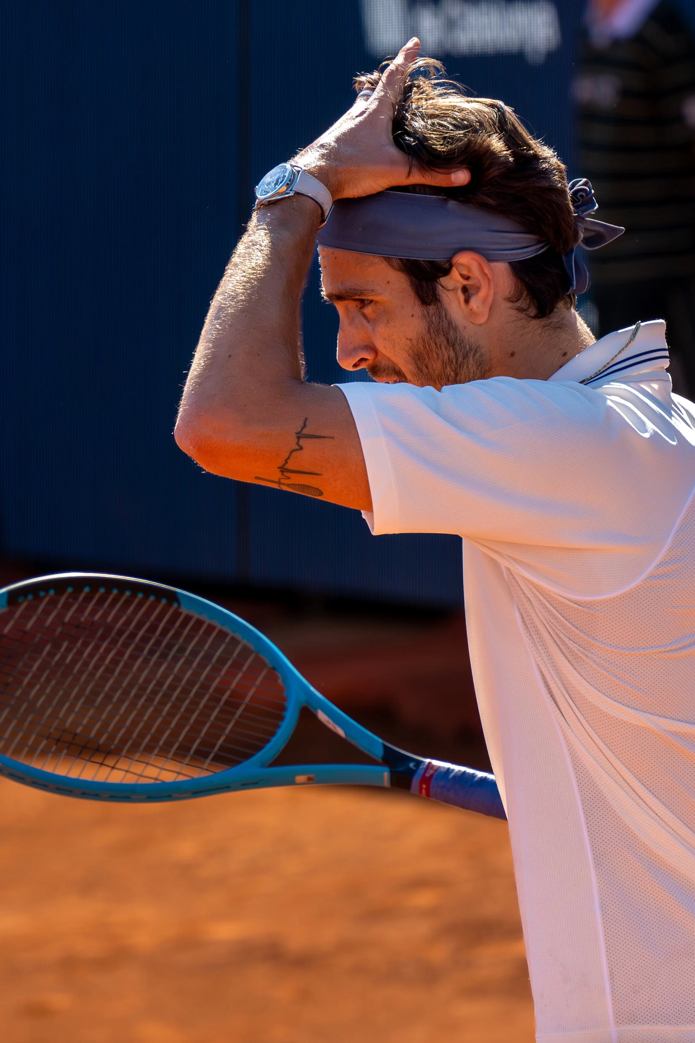Lorenzo Musetti holding his head with his hand during a match on a clay court.