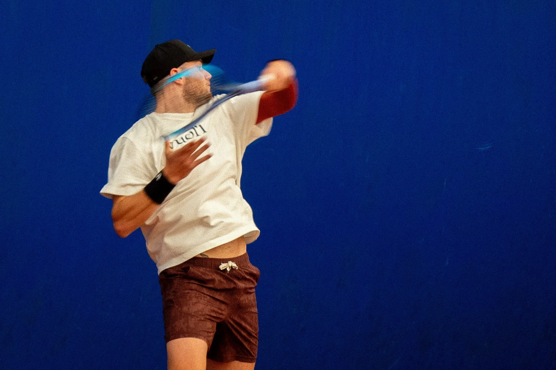 Person playing tennis hitting a ball with a racket in front of a blue background.