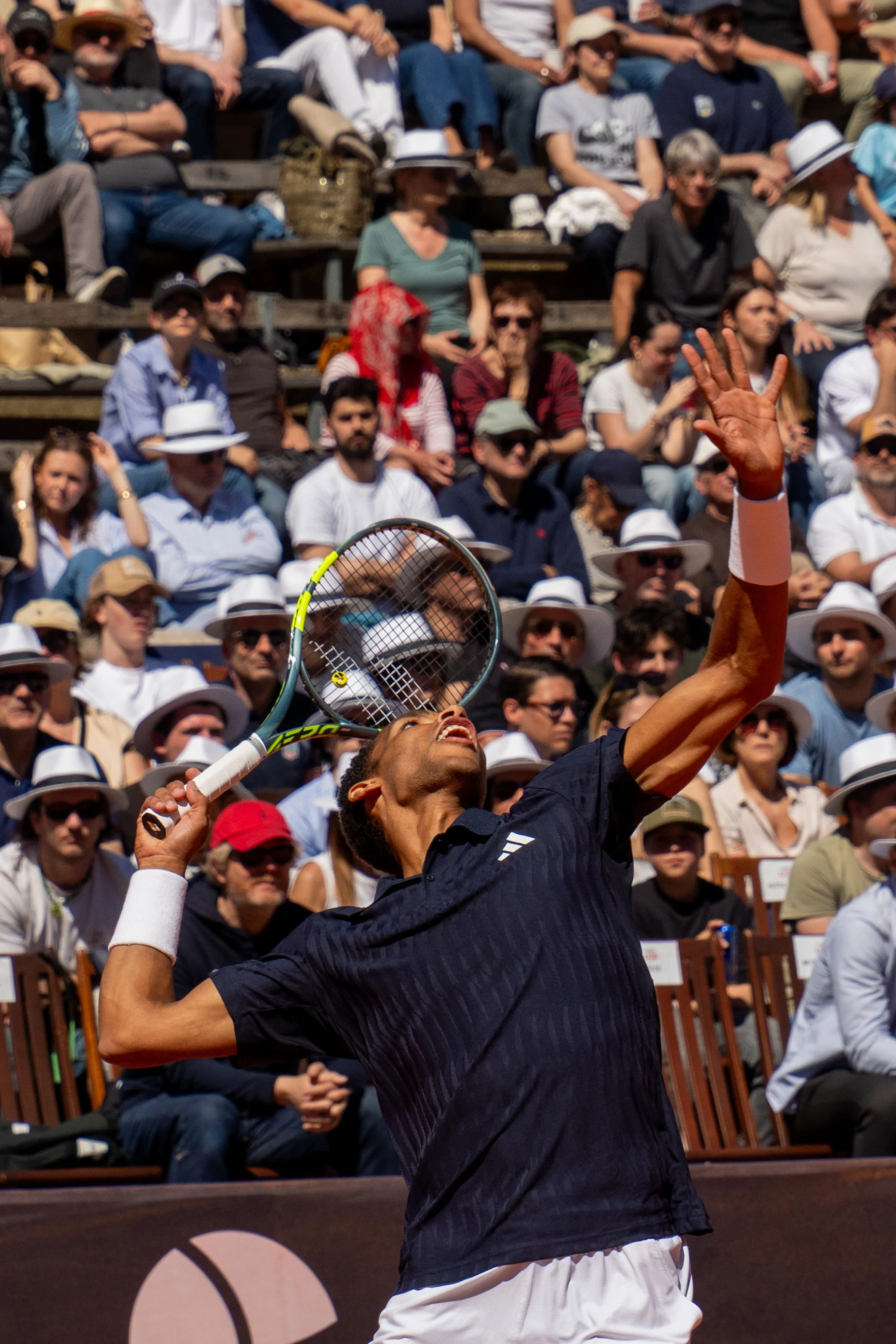 A tennis player serving on court with a large crowd of spectators in the background.