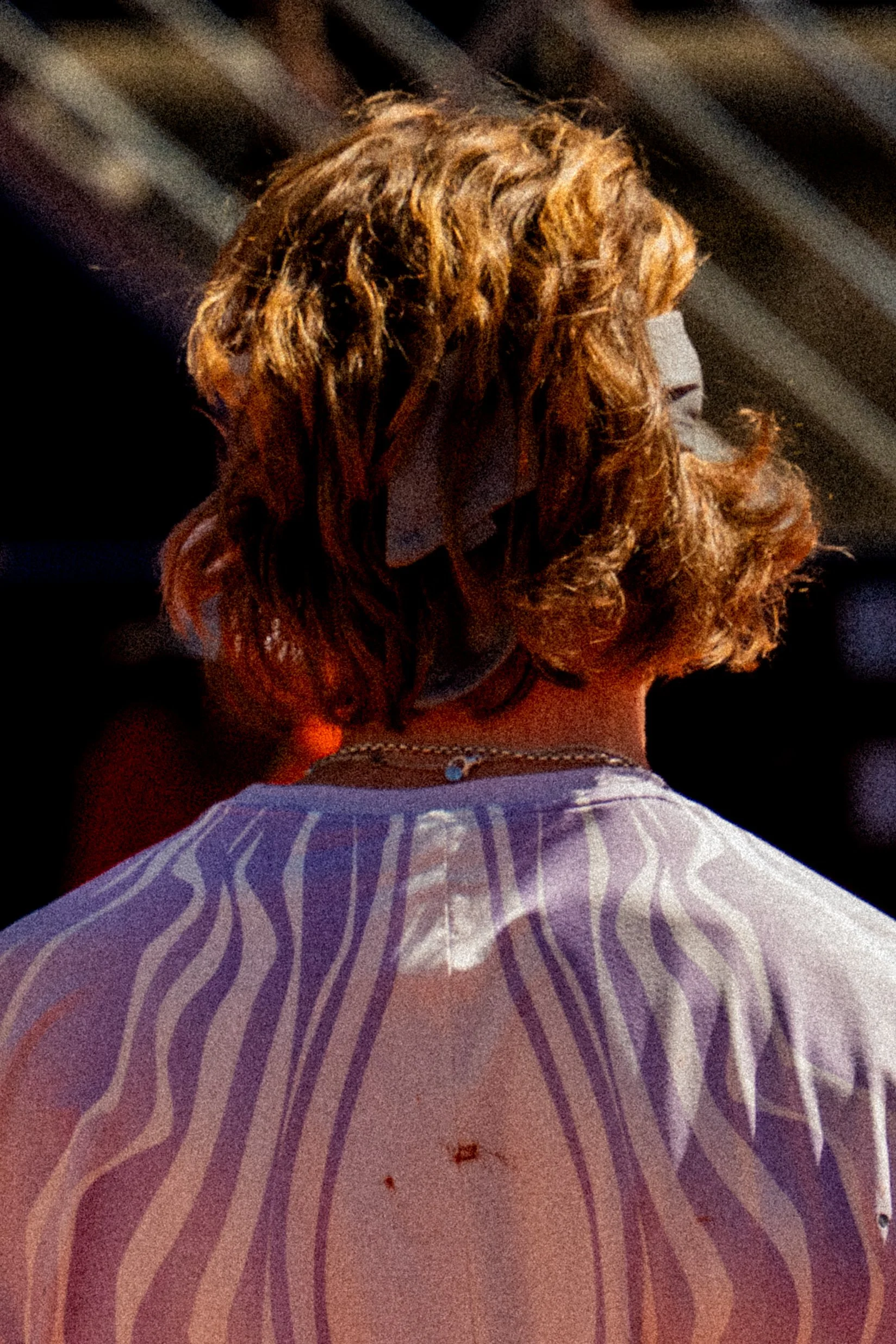Back view of a woman with curly blond hair, wearing a striped shirt with some dirt or stains on the back.