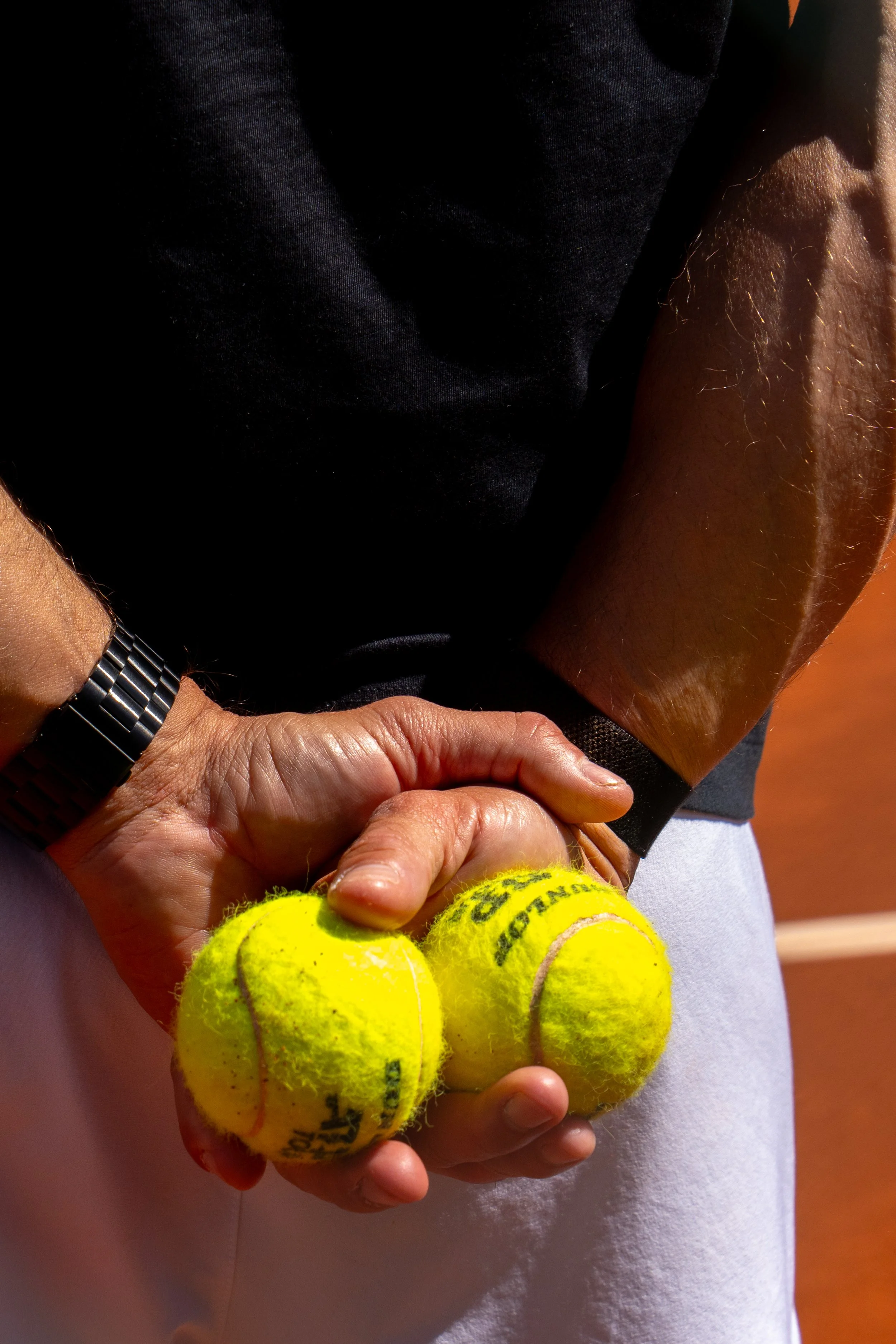 Close-up of a person holding three yellow tennis balls with black writing, with the person's arm and hand visible, wearing a silver watch.
