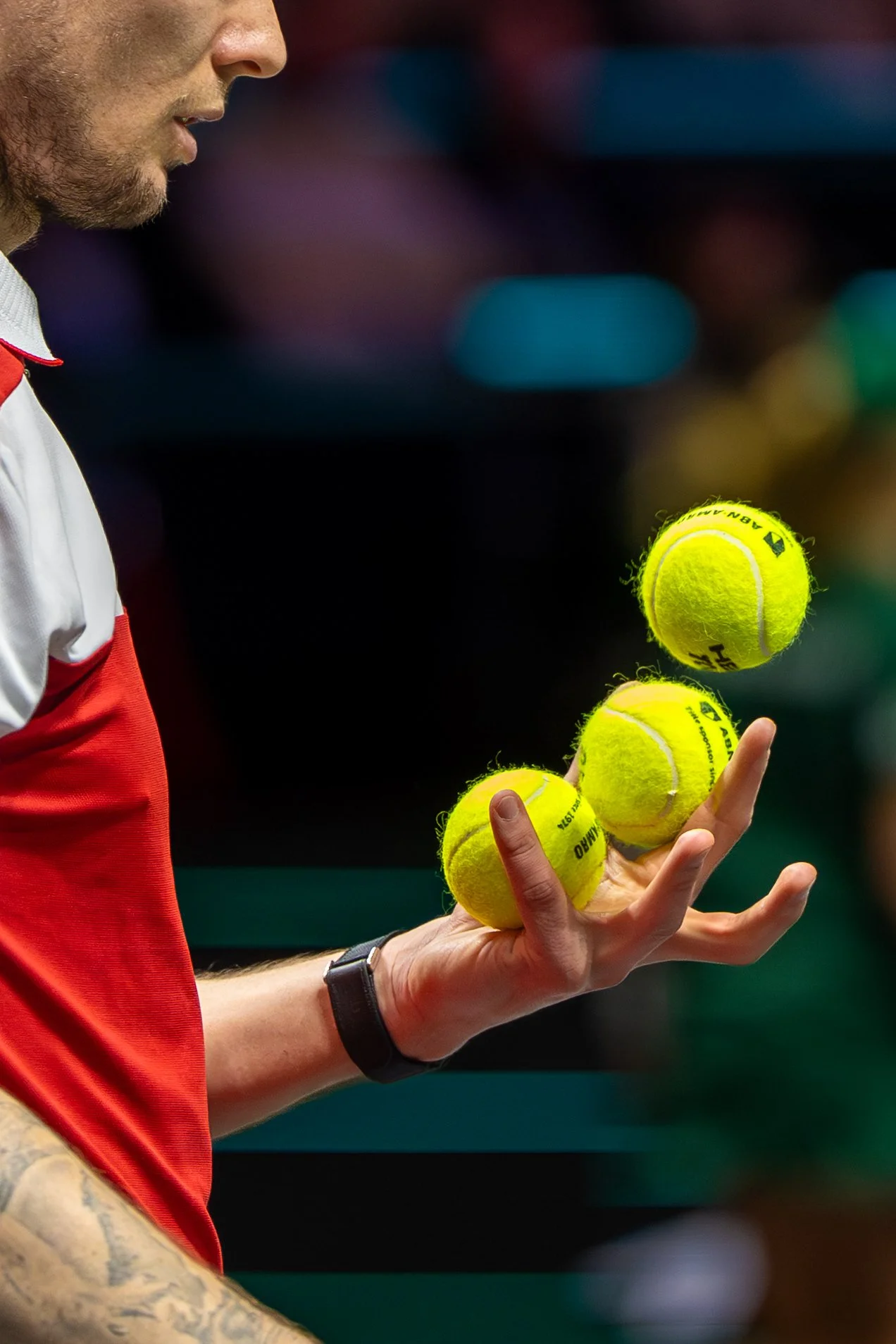 Alexander Bublik juggles three bright yellow tennis balls against a blurred indoor background.