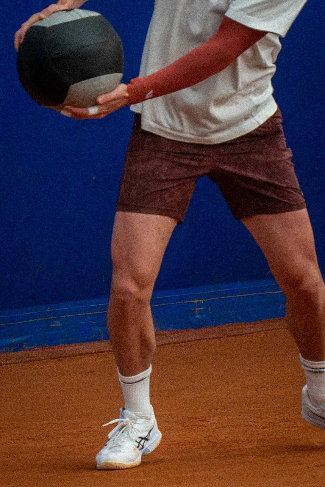 Person wearing athletic clothes holding a medicine ball on a gym floor.
