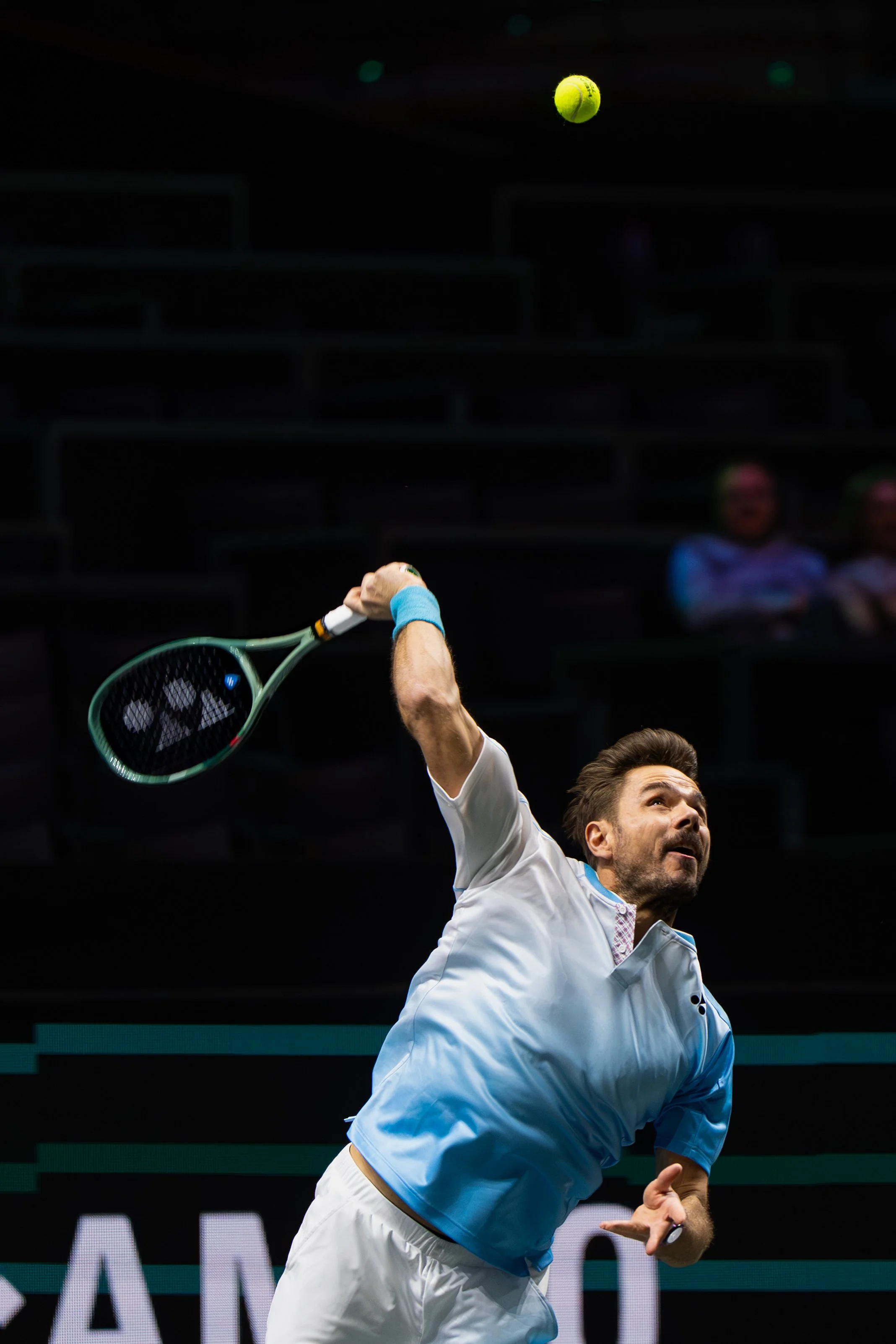 Stan Wawrinka in white and blue outfit serving a tennis ball with a tennis racket during a match.