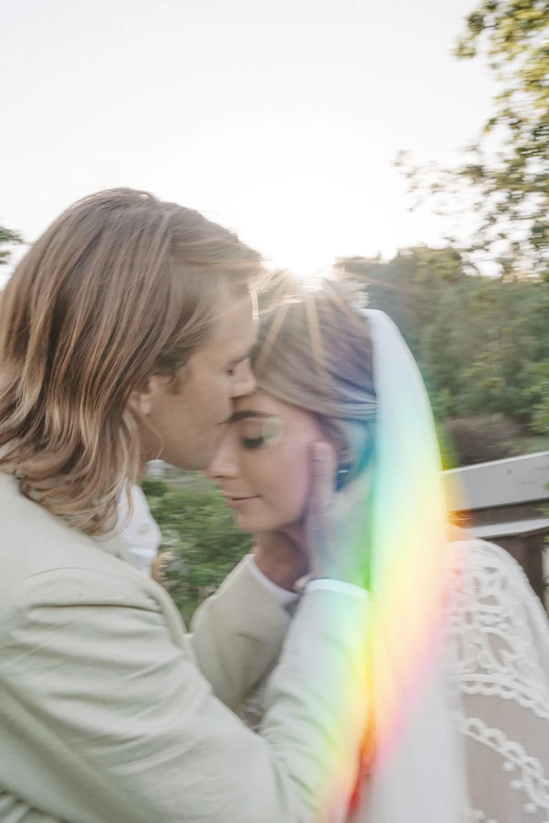 Two women embracing each other outside with sunlight and a rainbow lens flare.