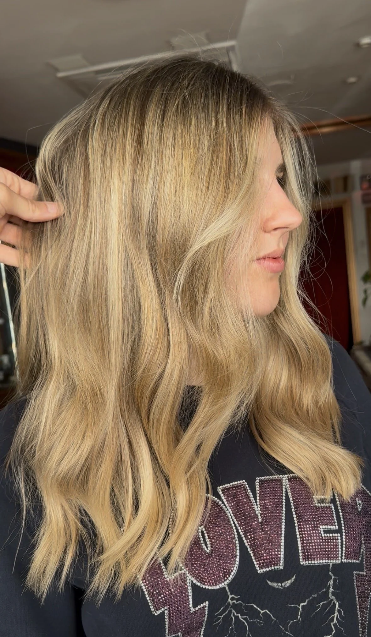 A woman with long, wavy blonde hair, seen from the side, wearing a black shirt with a glittery design.