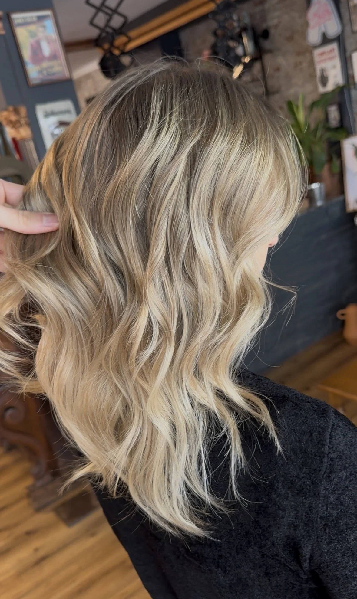 Side view of a woman with blonde, wavy hair, sitting in a salon.