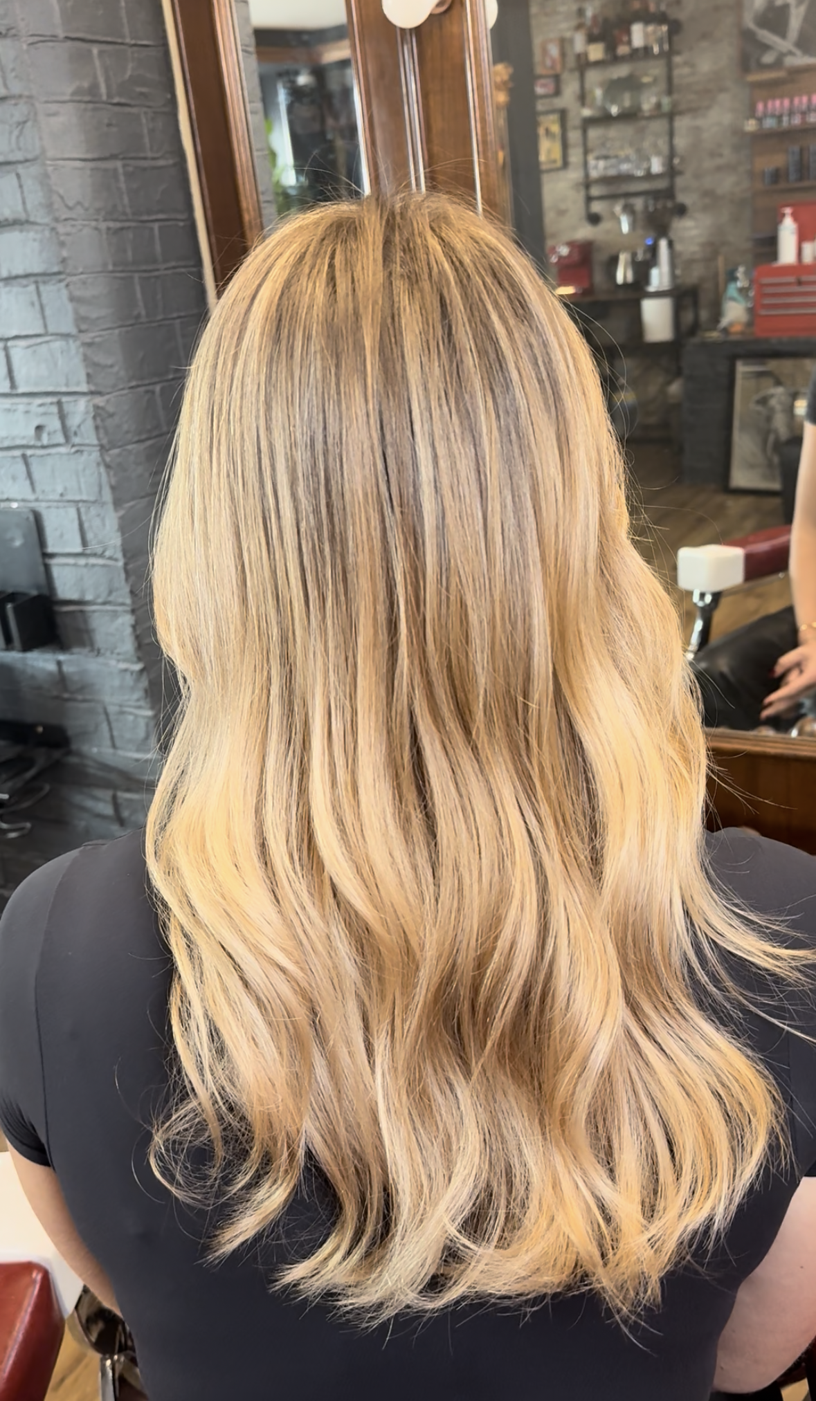 Woman with long, wavy, blonde hair sitting in a salon chair.