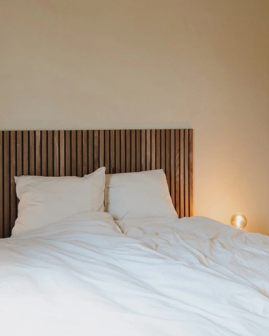 Social media management, content creatie voor vakantiehuis. Een bed met witte lakens en kussens, houten hoofdbord, en een zachte lamp aan de rechterkant.