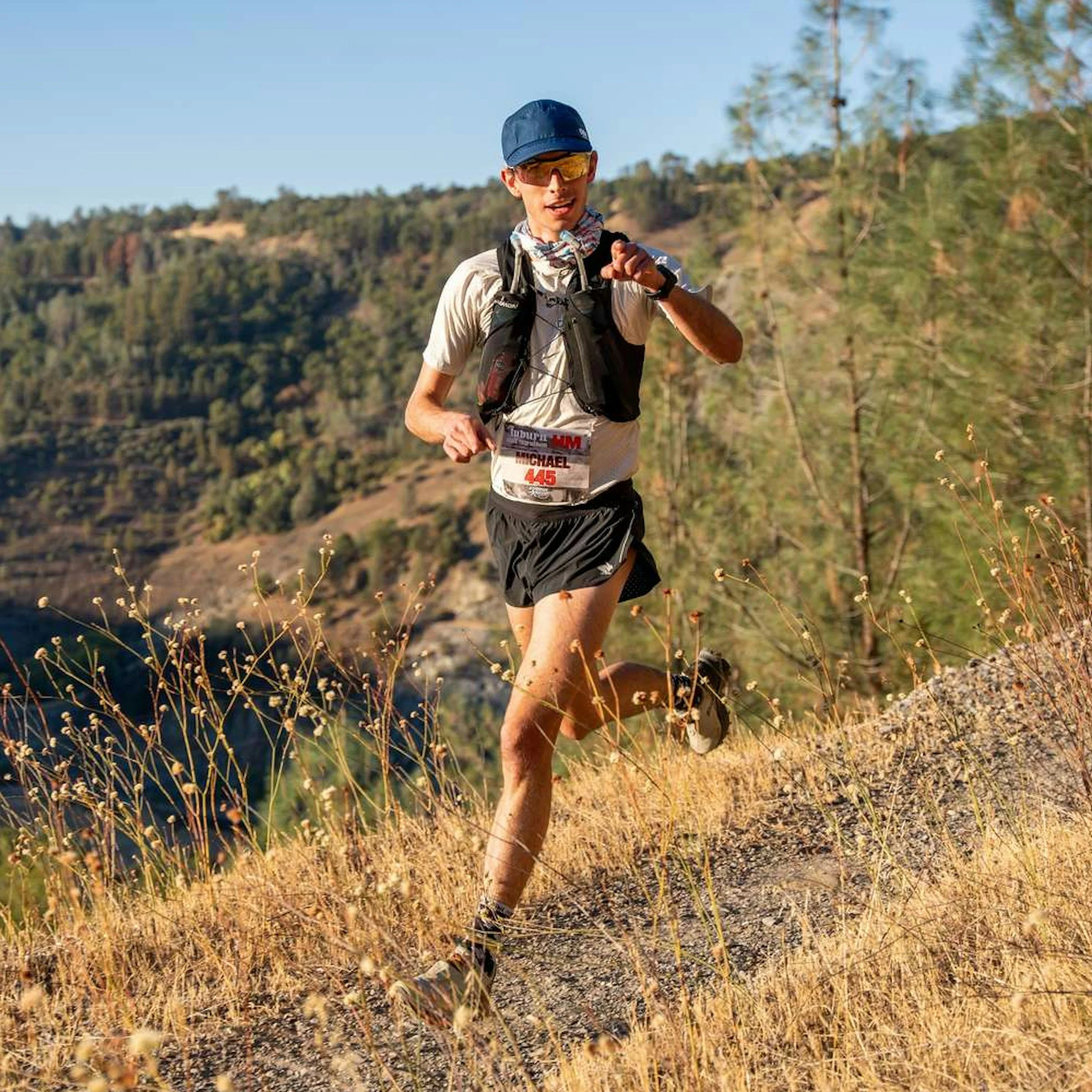Trail runner wearing hydration vest running on a dry mountain path during a race