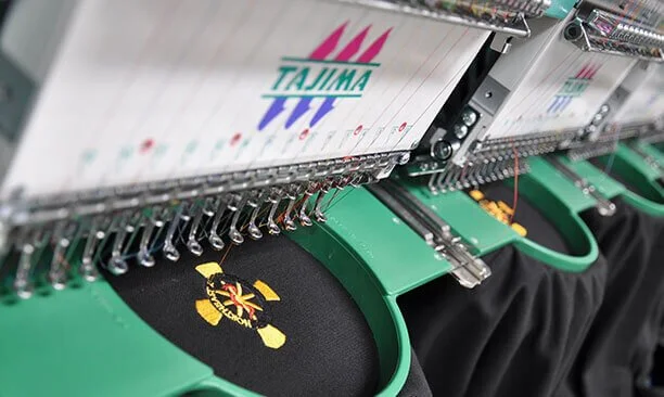 Embroidery machine stitching a colorful logo onto black fabric.