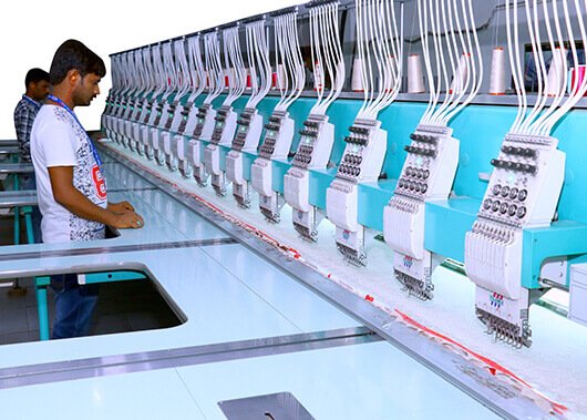 Two people operating industrial embroidery machines in a textile factory.