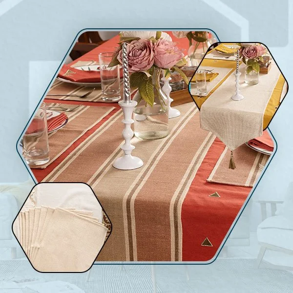 A table set for a meal with a beige and rust-colored striped tablecloth, pink roses in a glass jar, clear drinking glasses, white candlesticks, and beige napkins.