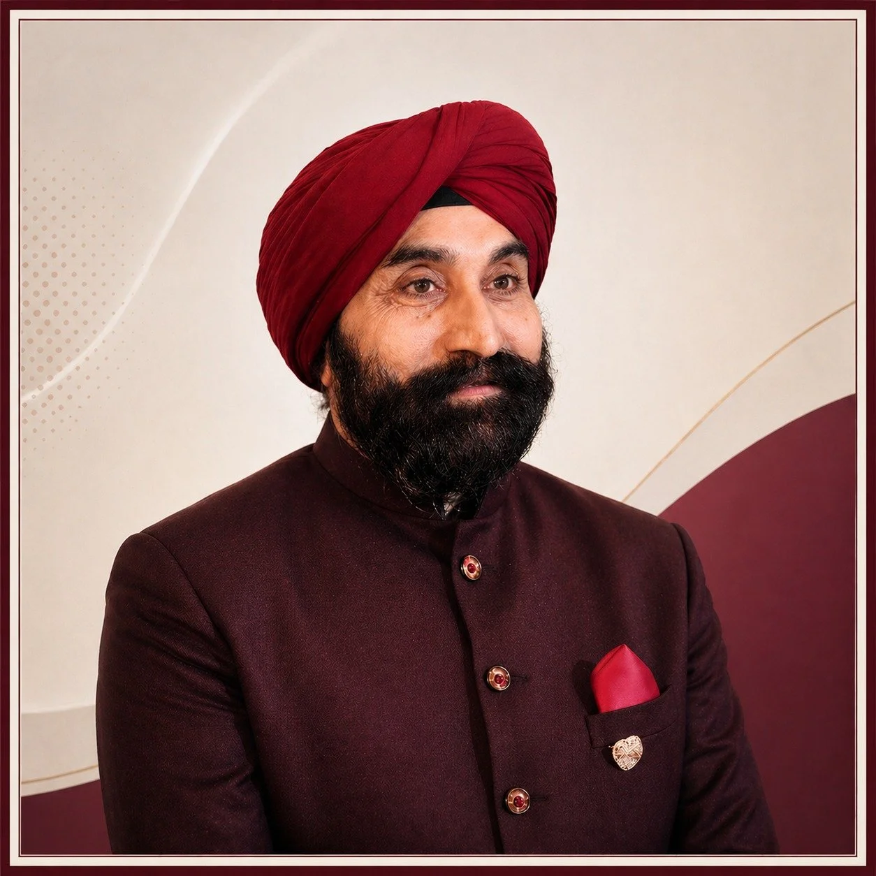 Man wearing a maroon traditional Indian suit with a matching turban and a red pocket square, posing against a decorative beige and maroon background.