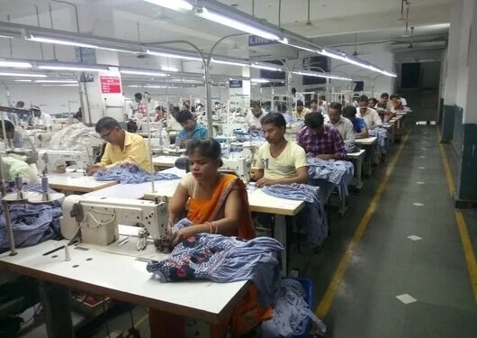 Workers sewing on industrial sewing machines in a large factory.