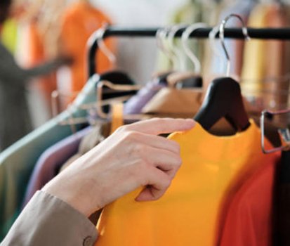 Close-up of a hand browsing colorful shirts on a clothing rack in a store.