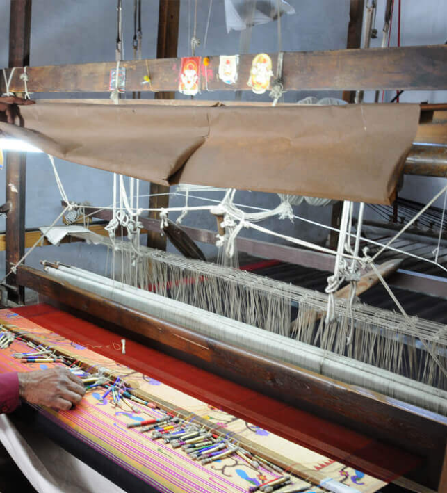 Close-up of traditional handloom weaving machine with colorful threads and completed woven fabric in bright colors and patterns.