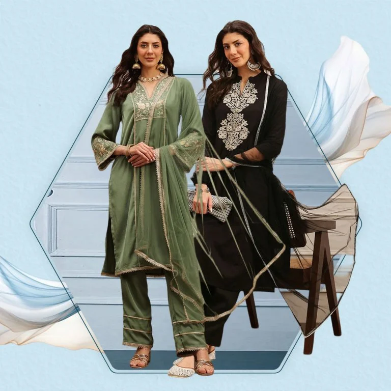 Two women standing side by side in traditional South Asian attire. The woman on the left wears a green embroidered salwar kameez with matching pants and gold jewelry. The woman on the right wears a black outfit with silver embroidery, holding a clutch. They are in a minimalist room with light blue walls and a wooden bench, with artistic fabric-like designs in the background.