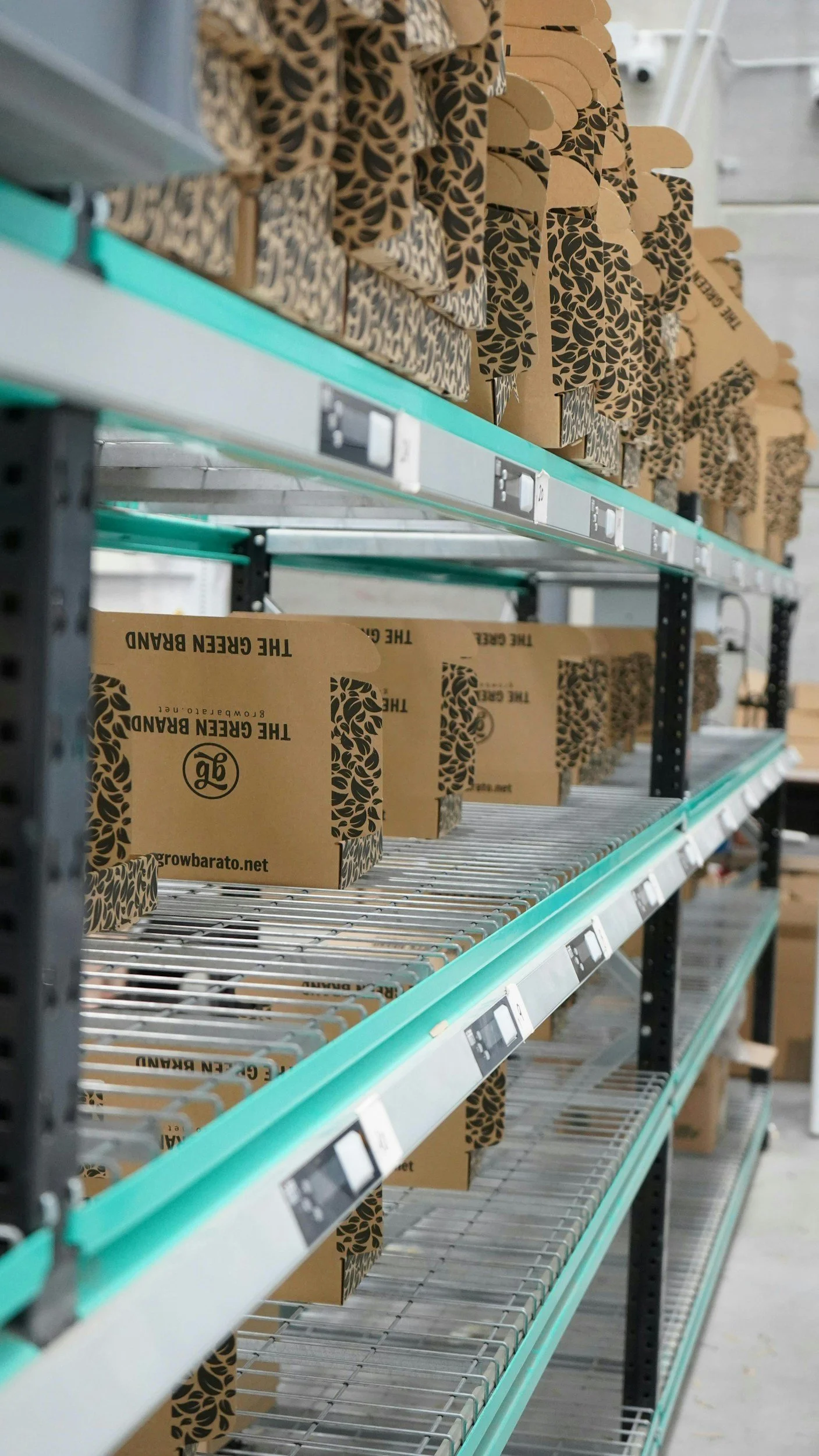 Empty store shelves with a few cardboard boxes labeled 'The Green Brand' and 'growbarato.net,' in a warehouse or retail environment.