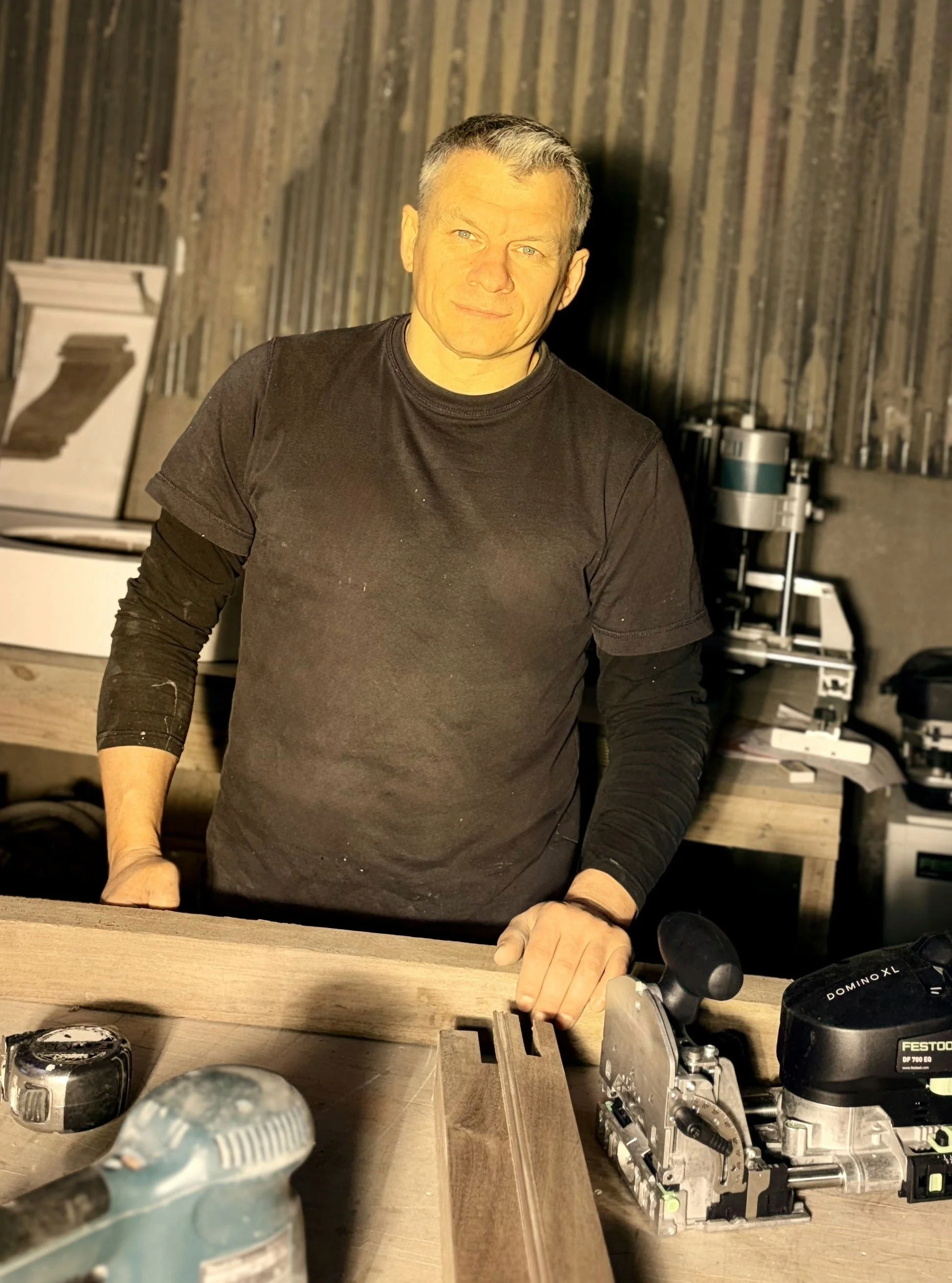 Juris Martinovs, founder of Remesis Ltd, in his joinery workshop with tools and bespoke timber work in progress.