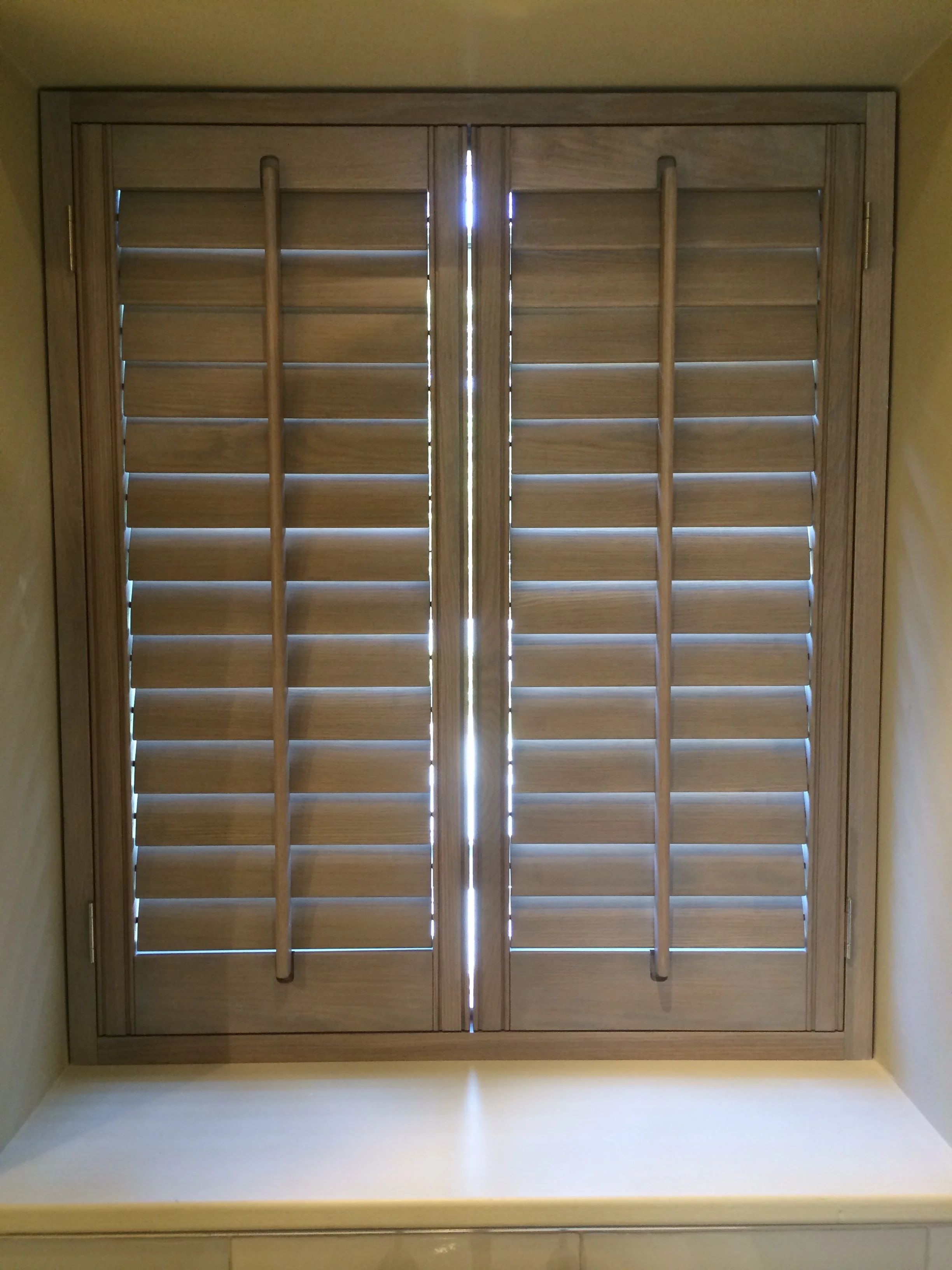 View of closed wooden shutters with horizontal slats and vertical handles, allowing light to peek through gaps.