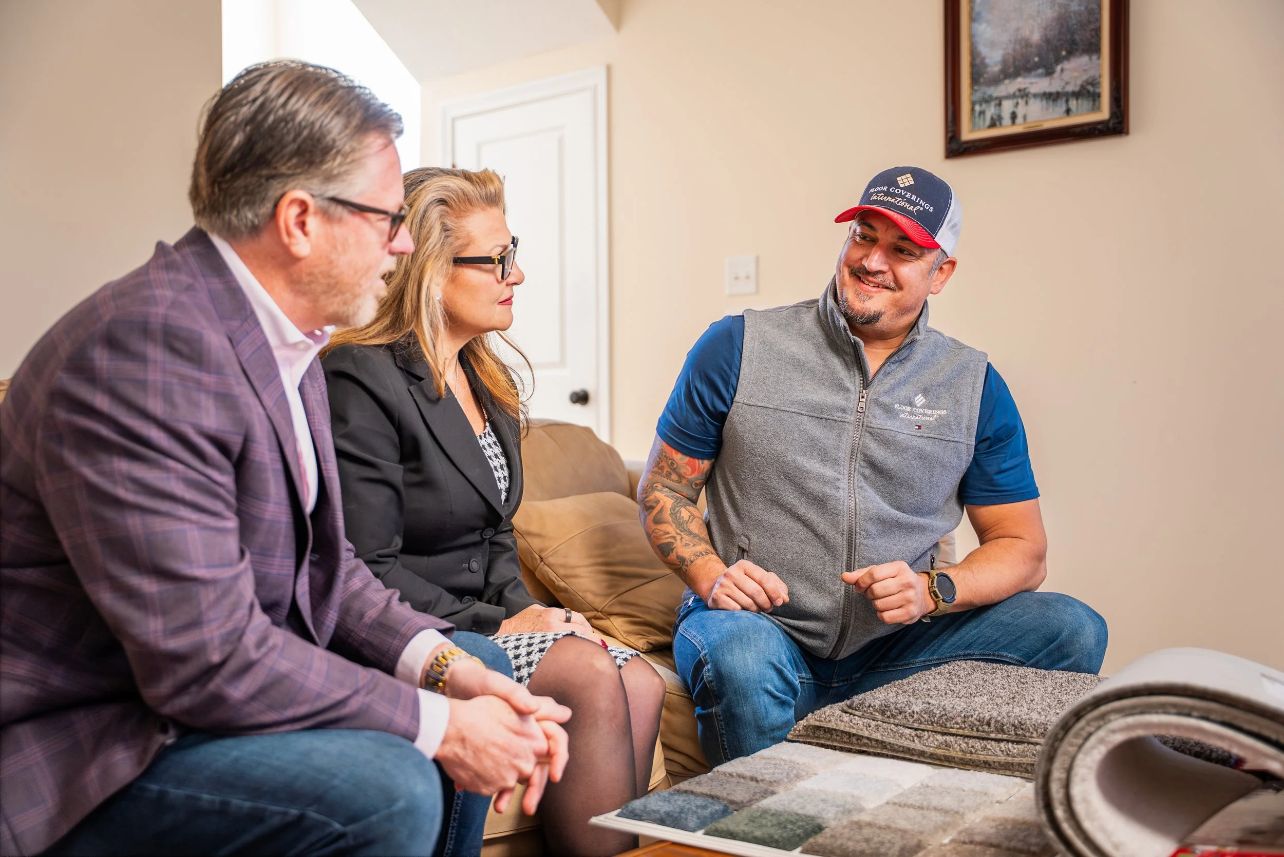 Four people sitting on a couch in a home, discussing flooring samples displayed on a table in front of them.