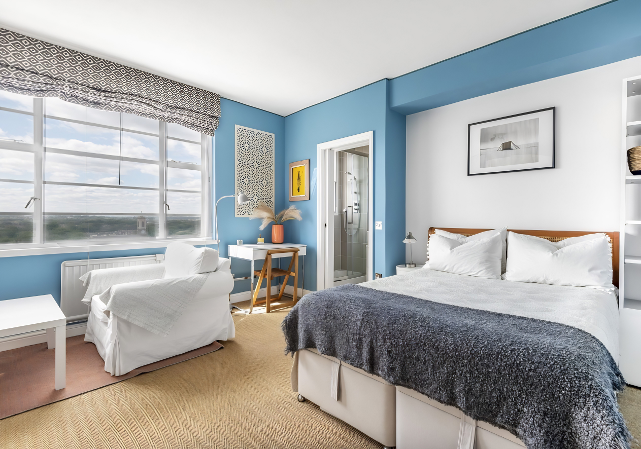 Blauwe slaapkamer met tweepersoonsbed, fauteuil en groot raam