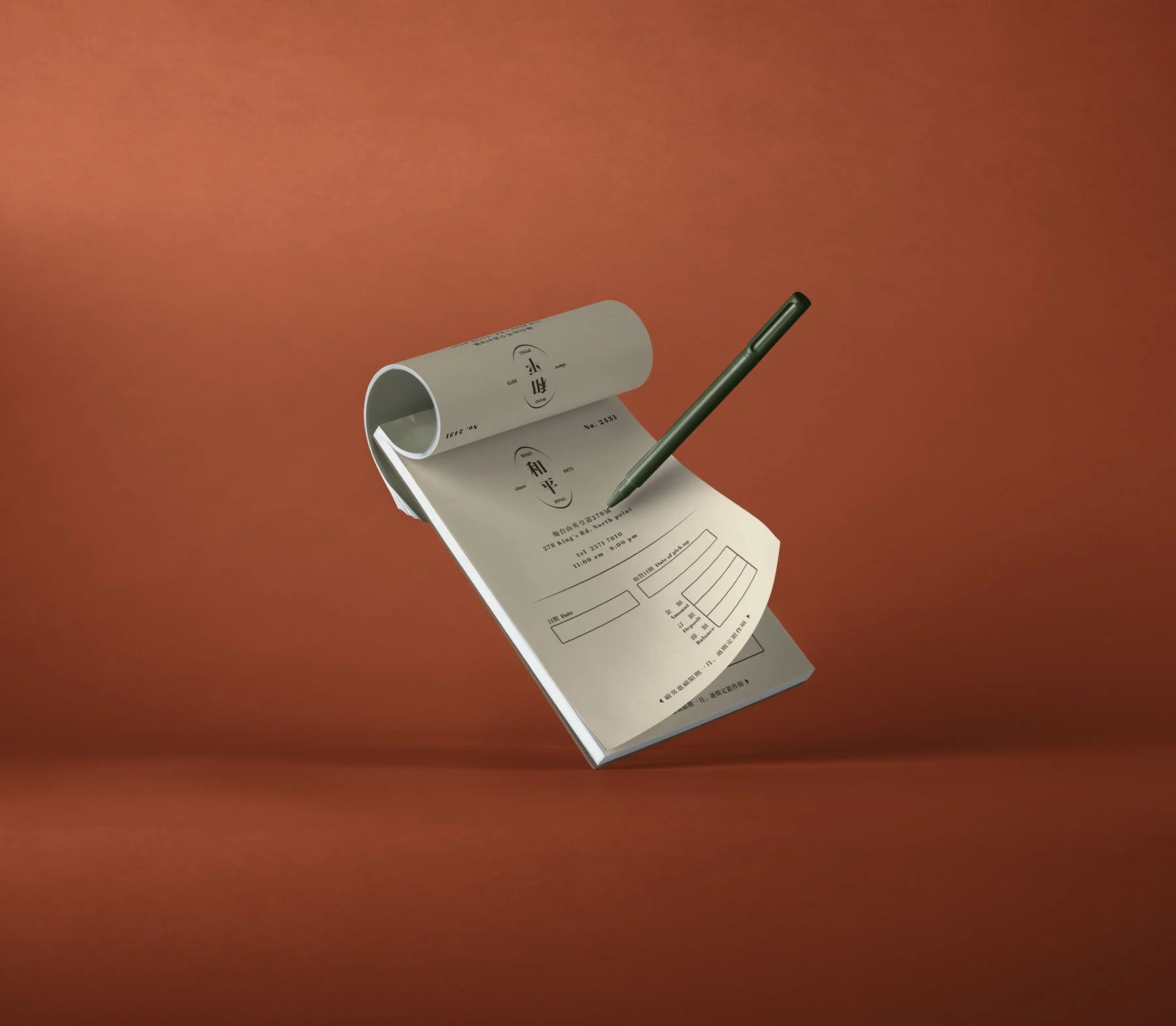 A notepad with Japanese writing and charts, a green pen, and a rolled-up sheet on a plain reddish-brown background.