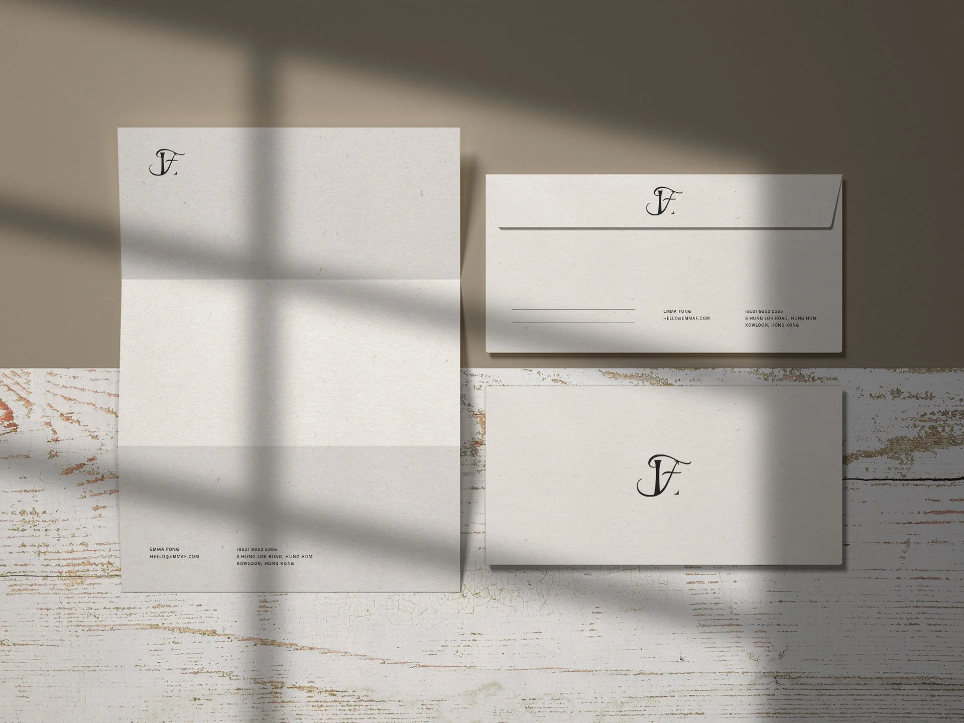 Set of stationery including letterhead, envelope, and folded card with monogram 'F', on a white wooden surface with natural light and shadows.