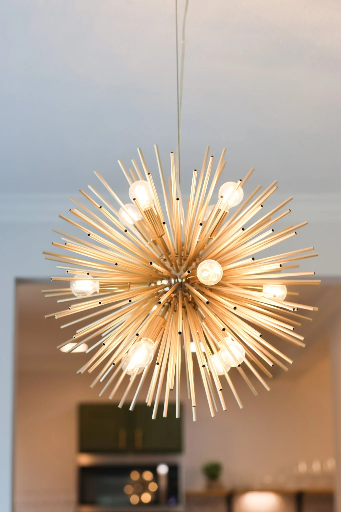Modern chandelier with multiple radiating metal rods and exposed bulbs hanging from the ceiling in a living room.