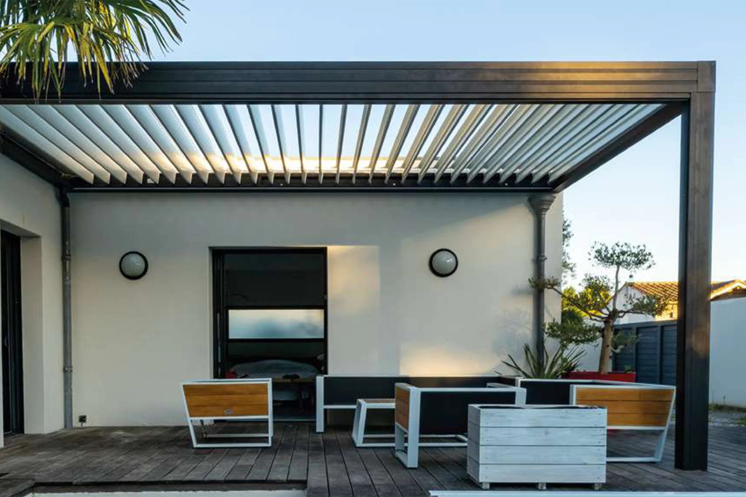 Moderne Terrasse mit Sitzgruppe, Holzdecke und Markise, Balkon mit Garten und Bäumen im Hintergrund bei Sonnenuntergang.