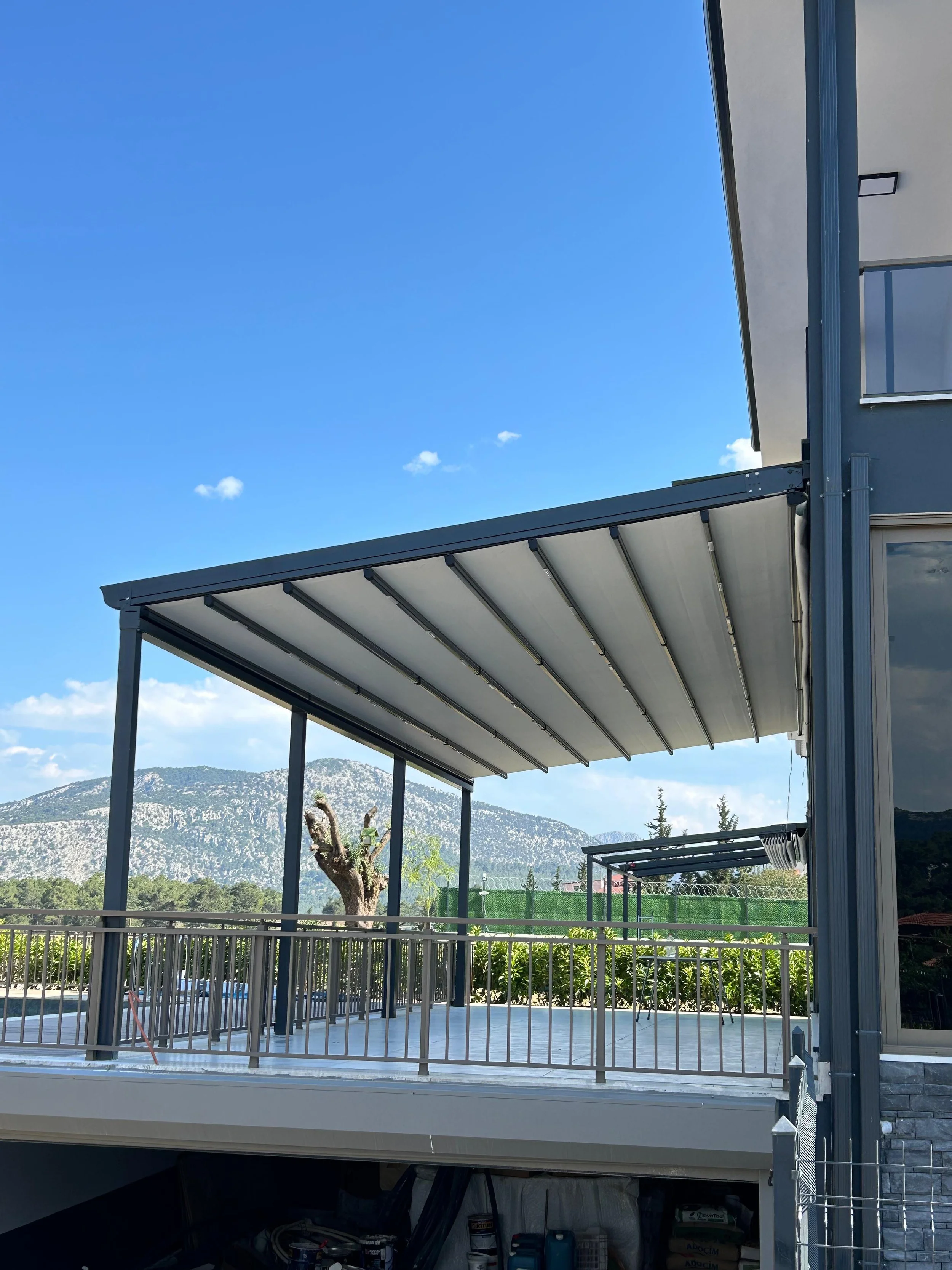 Moderner Balkon mit Markisen vor einer Bergkulisse bei blauen Himmel.