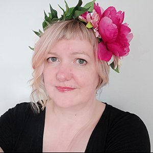 Woman with short blonde hair wearing a black top and a flower crown with pink flowers and green leaves.